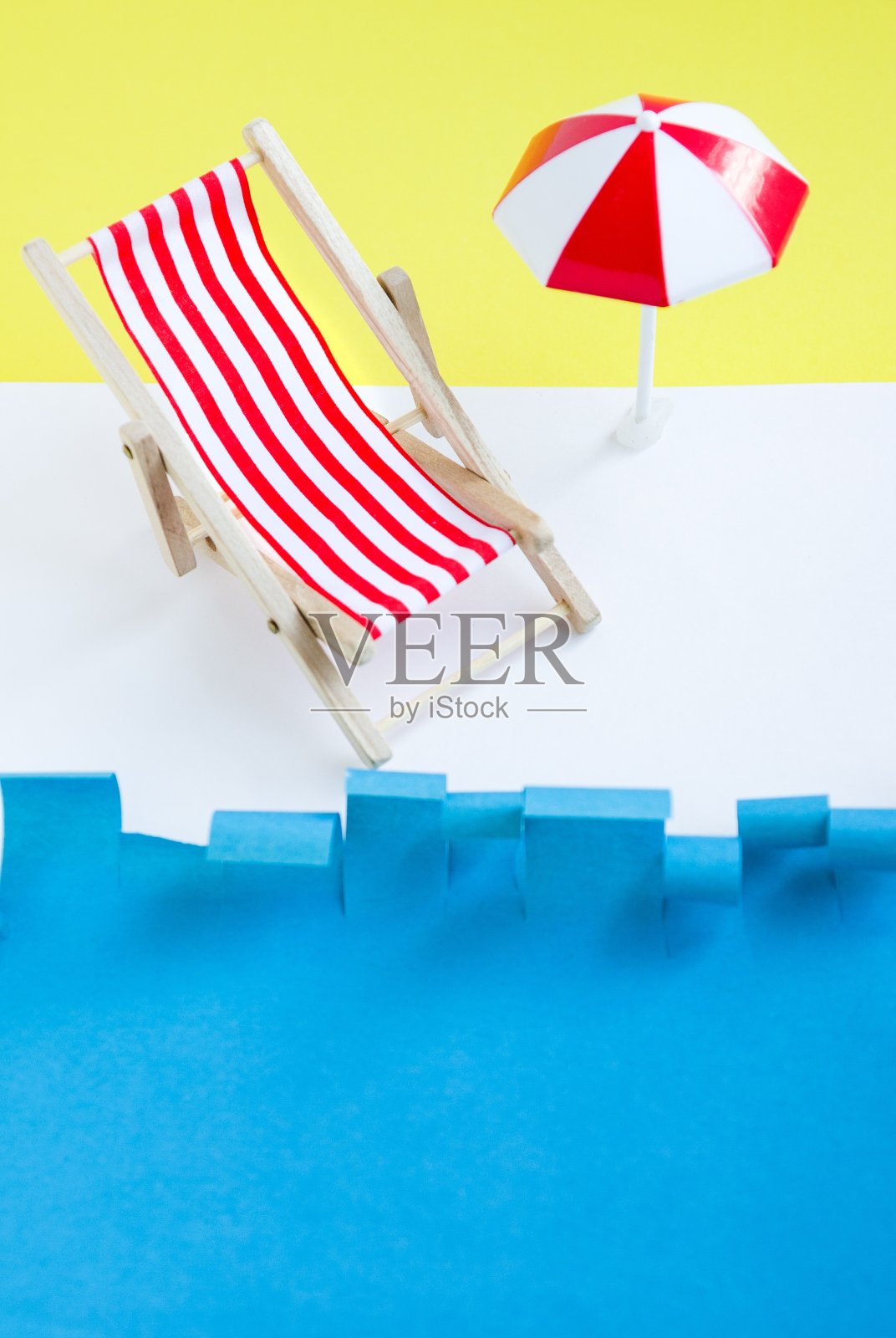 靠近海边的带伞的红色躺椅。蓝色和黄色背景的玩具躺椅。概念夏天休息。照片摄影图片