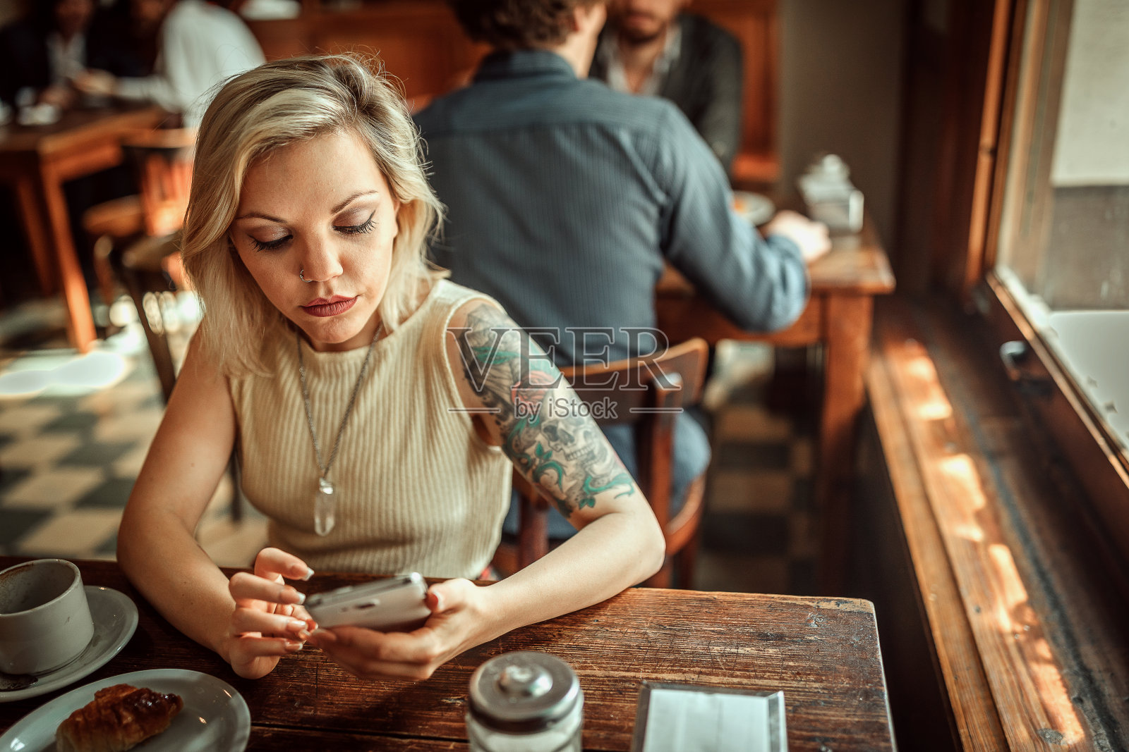 金发女人独自坐在当地的酒吧里，上网等待一个朋友照片摄影图片