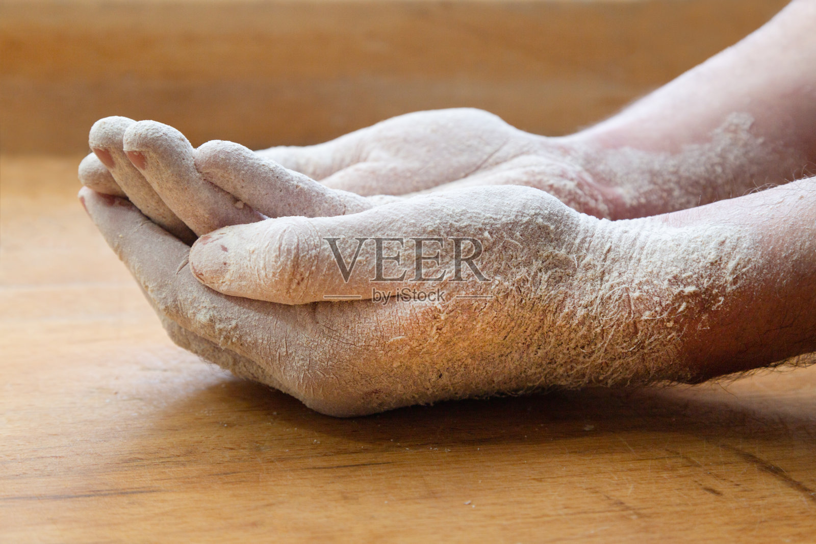 一个面包师傅的两只手的特写，上面覆盖着面粉，放在一张木桌上照片摄影图片