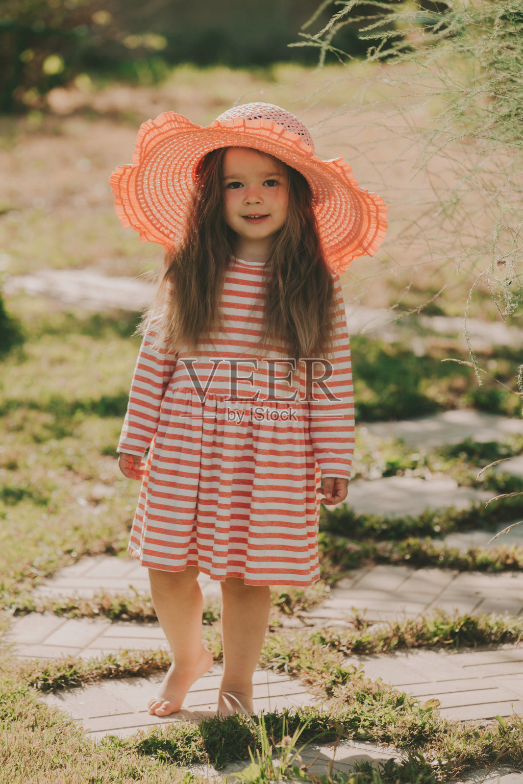 女婴穿着条纹连衣裙，戴着一顶粉红色的帽子。照片摄影图片