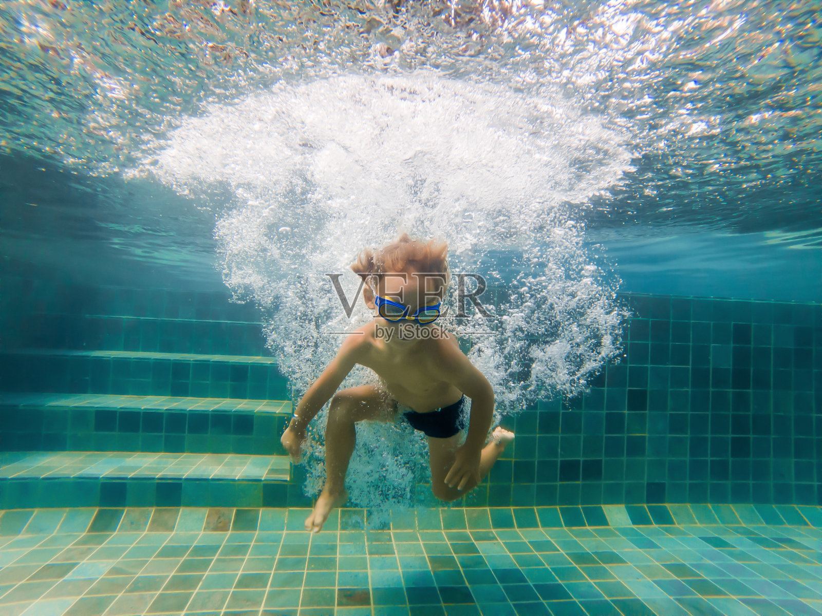 一个小男孩戴着游泳眼镜，微笑着屏住呼吸在游泳池里游泳照片摄影图片