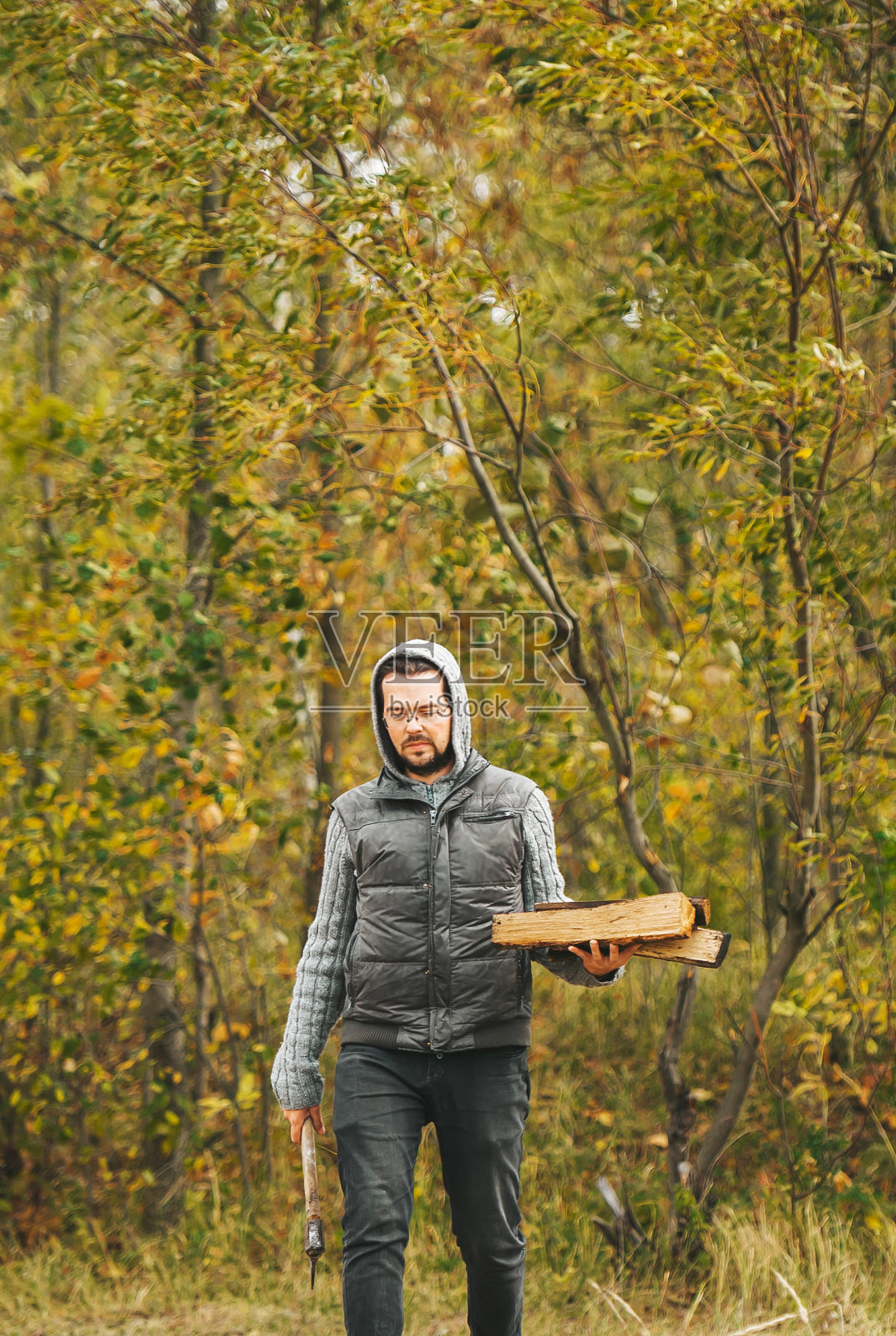 戴眼镜的男人拿着斧头。伐木工人拿着斧头在树林里照片摄影图片