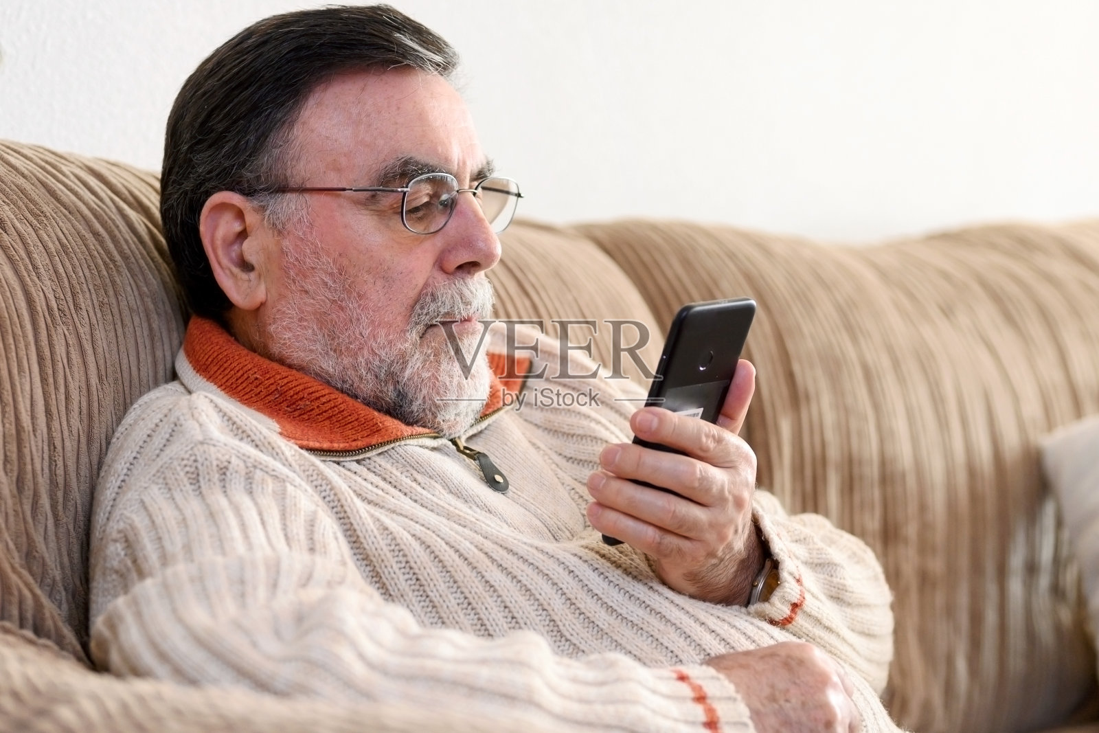 冠状病毒隔离期间，坐在家里沙发上使用手机的老人。照片摄影图片