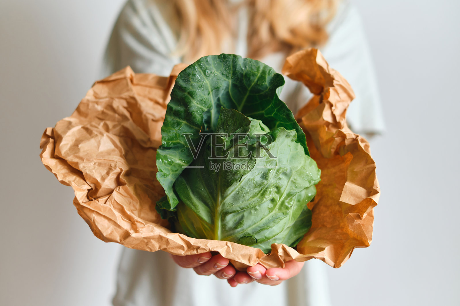 那个女人手里拿着小白菜。熟透的新鲜卷心菜纸包装。健康食品，有机蔬菜。天然维生素，食用原料。手工采摘的生物叶白菜照片摄影图片