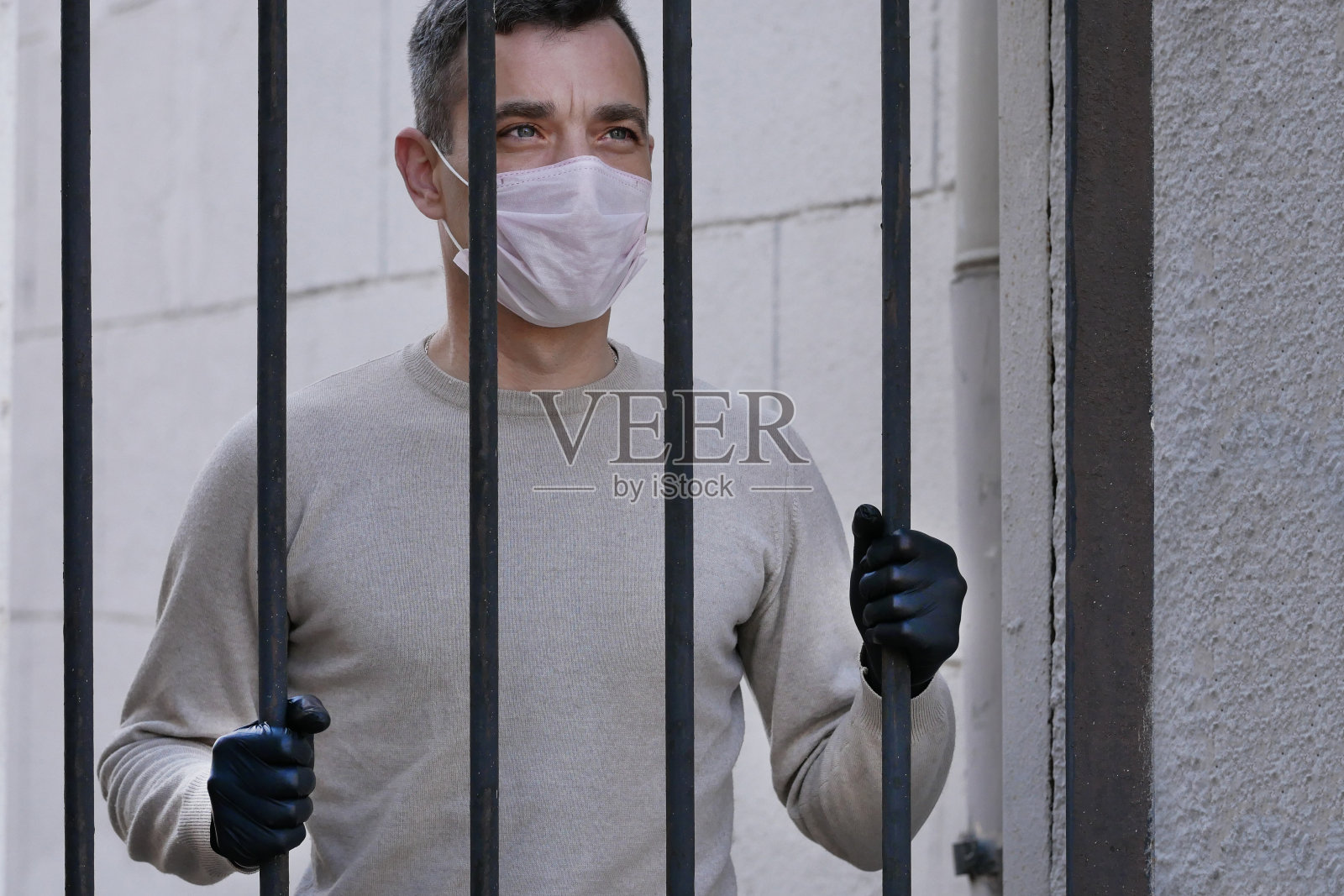 一名戴着白色防护面罩的男子靠近金属栅栏。隔离。冠状病毒的概念。戴防护面具和手套的人照片摄影图片