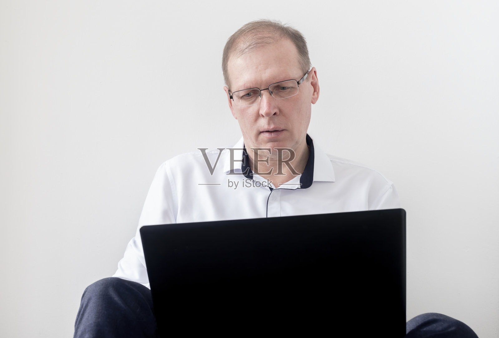 一个思想成熟的男人穿着西装坐在地板上，笔记本电脑在白色的背景孤立照片摄影图片