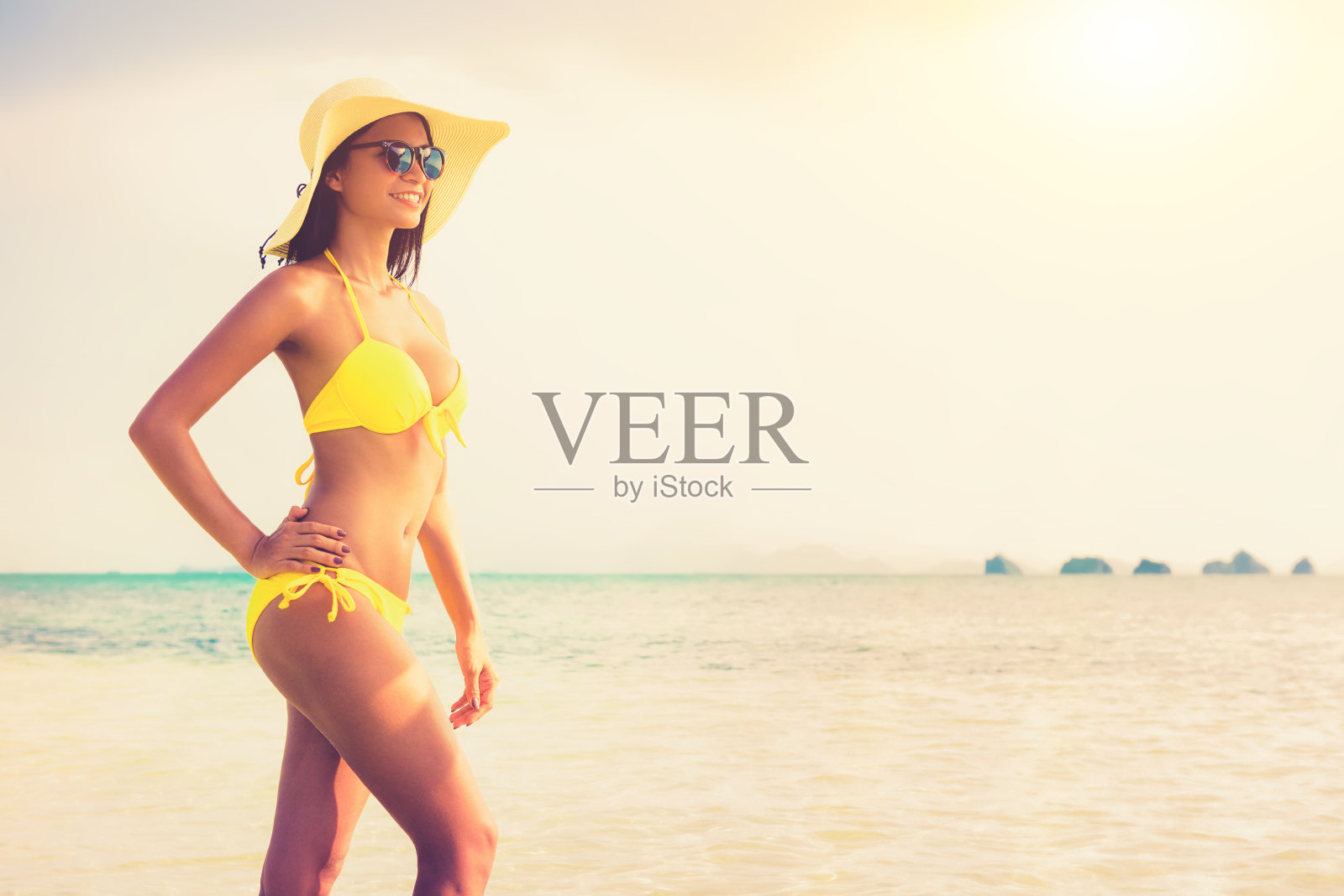 亚洲女人穿着黄色比基尼泳衣，太阳镜和帽子在夏天的海滩摆姿势照片摄影图片