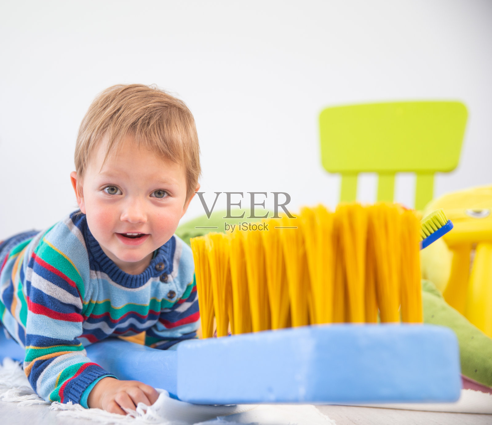 快乐的小男孩玩大牙刷复制品玩具看着相机在白色的背景-库存照片照片摄影图片