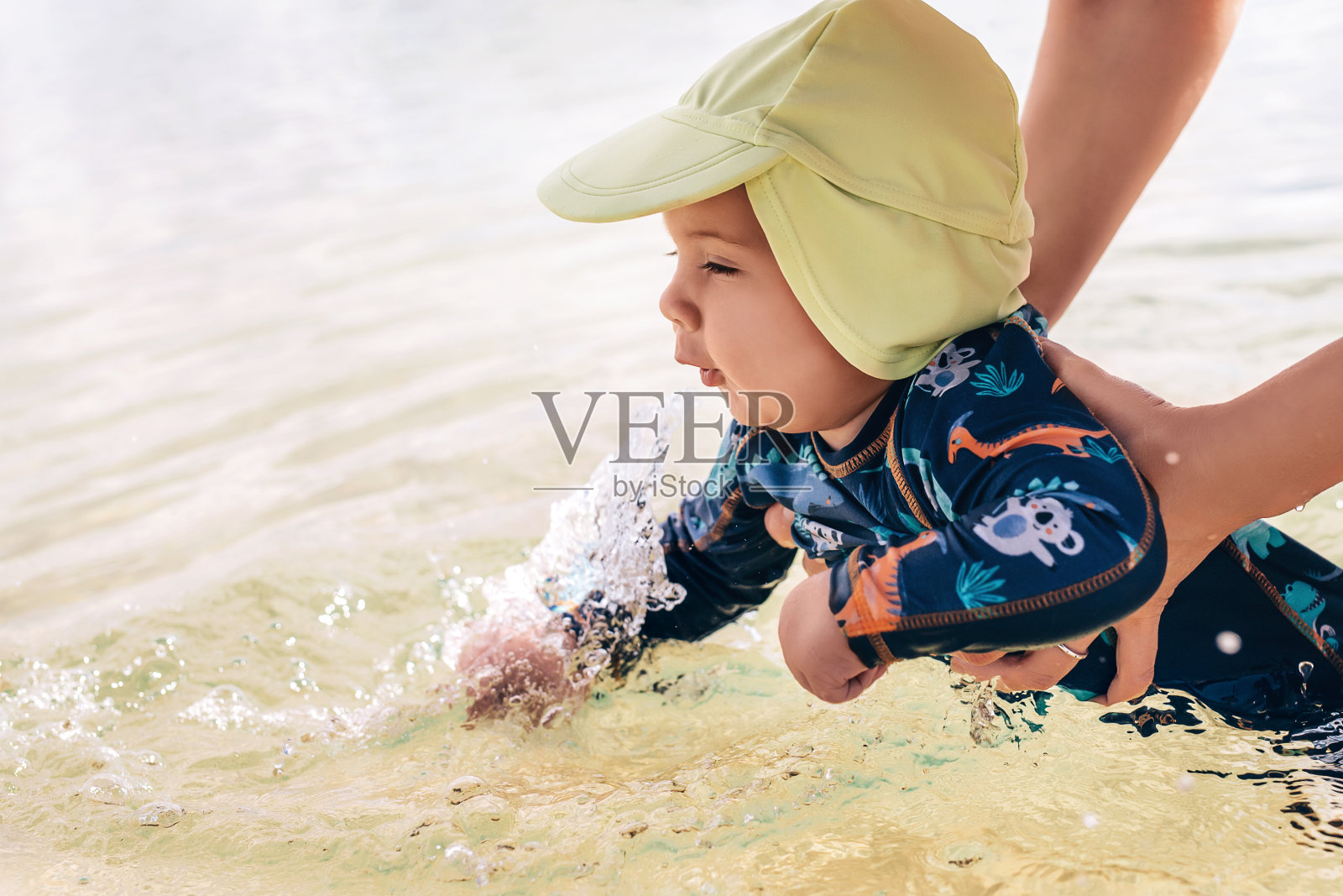 快乐的小宝贝小男孩在海里享受着自己的游泳，妈妈的手正牵着他照片摄影图片