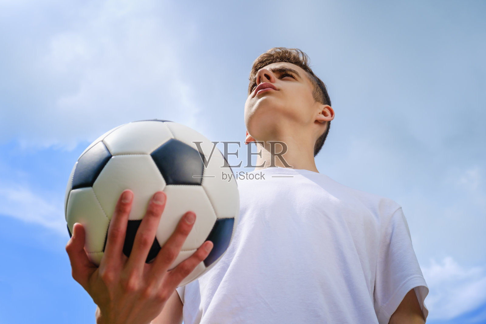 蓝天上一个拿着足球的少年照片摄影图片