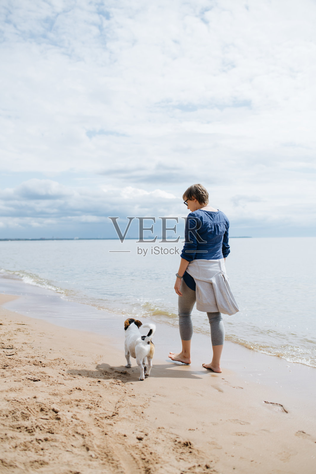 一个女人带着她的狗在沙滩上散步。后面的观点。照片摄影图片