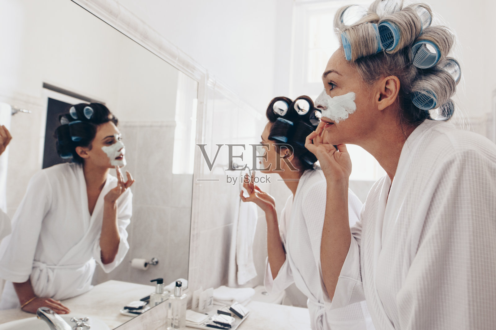 两个穿着浴袍的女人站在镜子前擦面霜照片摄影图片