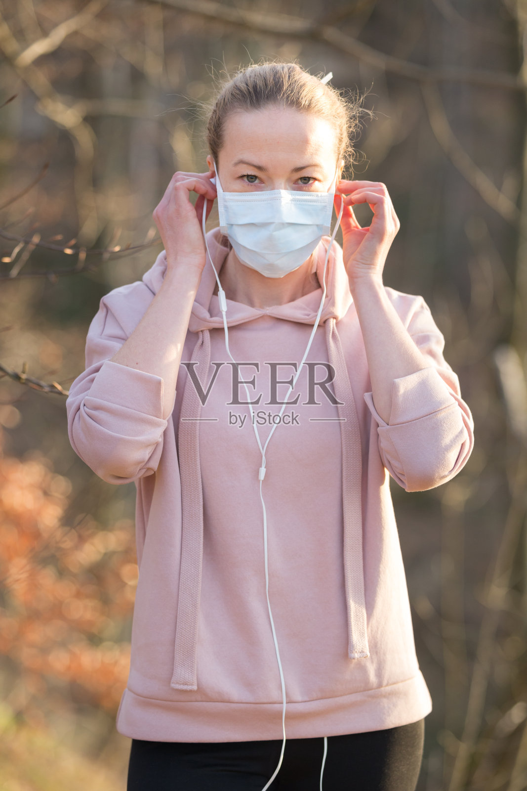 在公园里散步、放松和听音乐时，穿着医疗保护面罩的白人运动妇女的肖像。冠状病毒(Covid-19)正在全球蔓延照片摄影图片