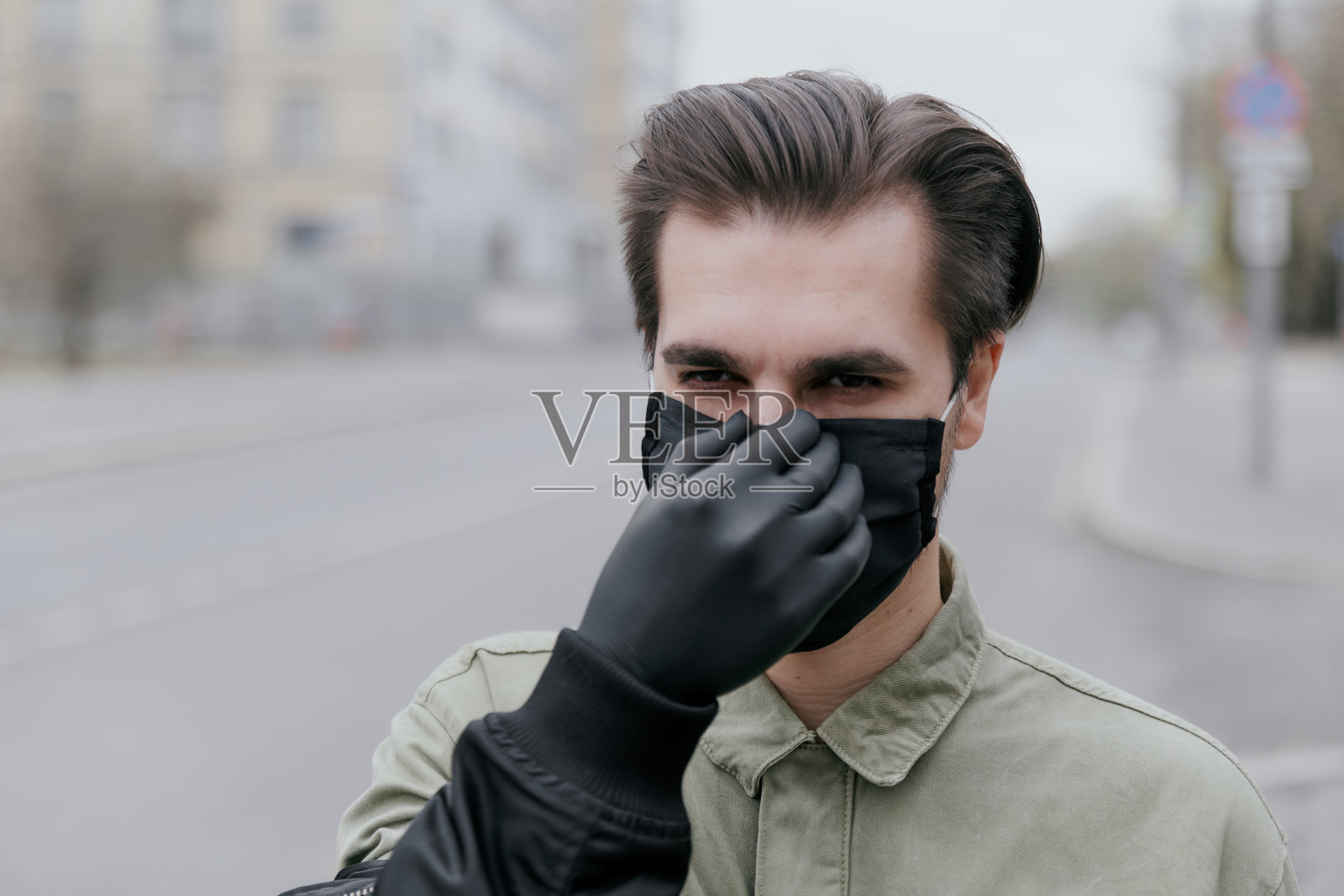 一个戴着黑色医用面具的男人的肖像。冠状病毒这个人用戴着黑色手套的手整理着他的面具照片摄影图片