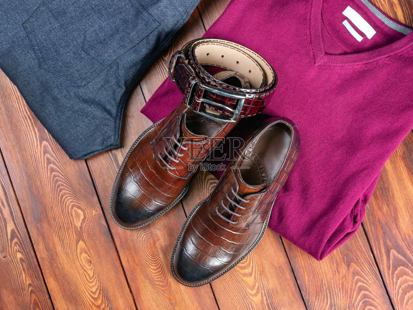 棕色鳄鱼皮鞋和裤带旁边的牛仔裤和套头衫在木板的背景照片摄影图片