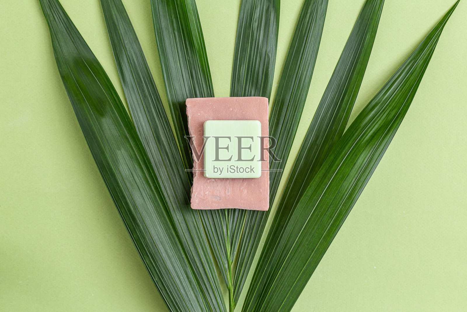 粉红色和绿色的天然香皂在棕榈树上。极简主义。静物画照片摄影图片