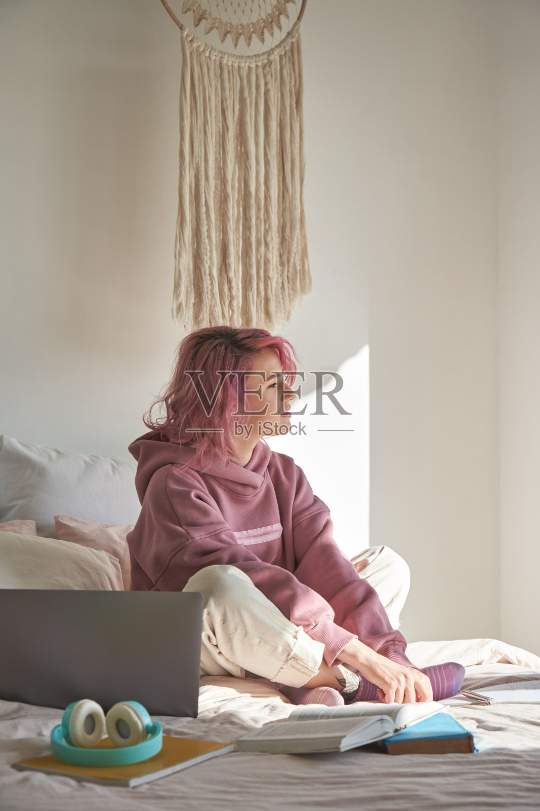 沉思沉思的青少年潮女粉红色的头发穿连帽衫坐在床上用笔记本电脑从学习中休息思考灵感转移目光，反思，梦想，感到忧郁陷入沉思。垂直照片摄影图片