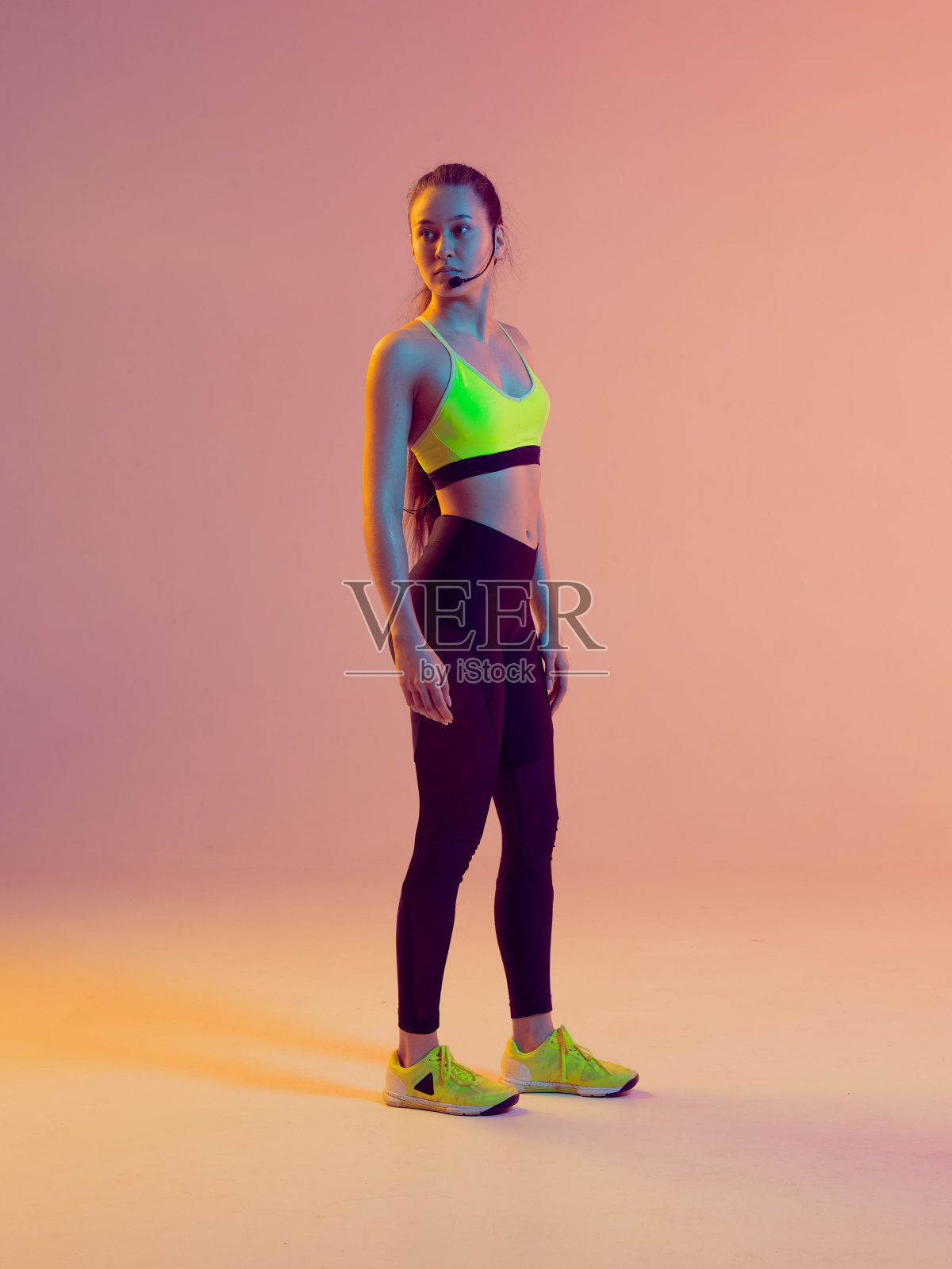 可爱的女孩健身教练戴着麦克风在网上健身，在一个霓虹灯背景。照片摄影图片