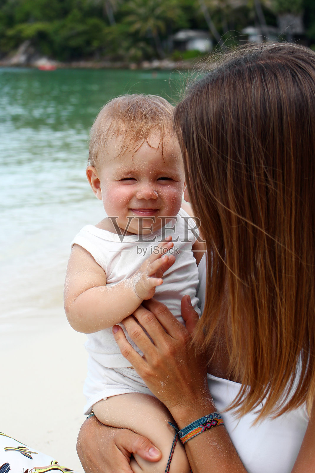 美丽年轻的欧洲母亲拥抱她的小女儿在热带海滩的背景。照片摄影图片