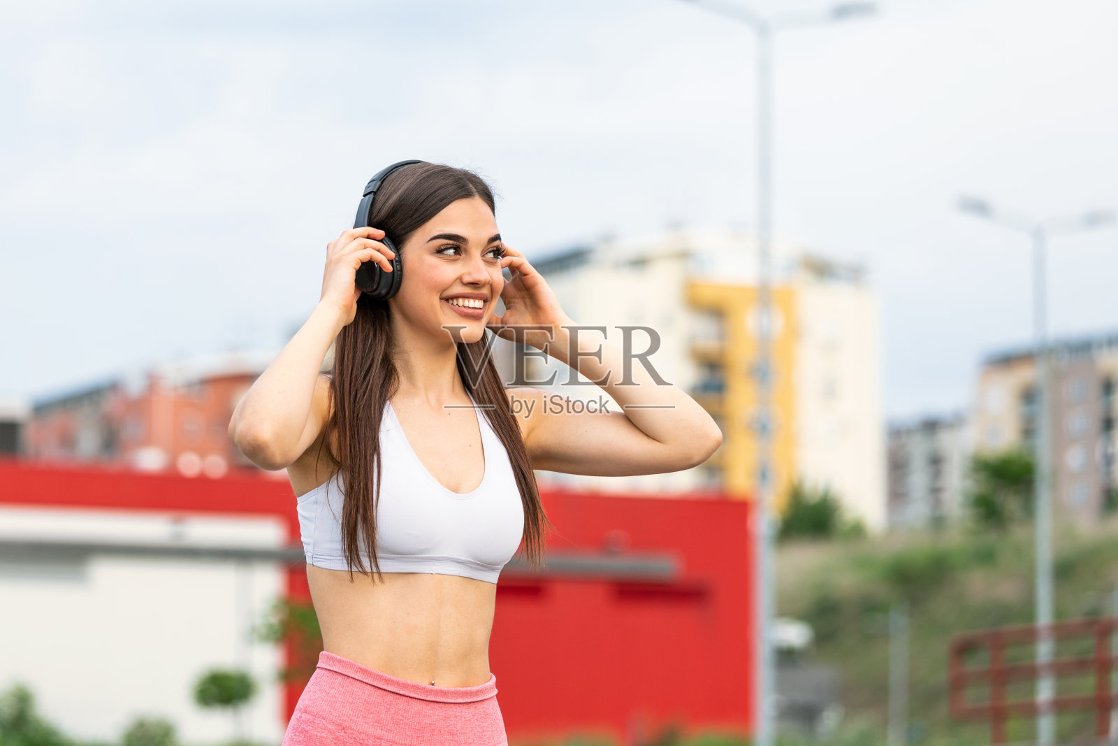 年轻女子一边跑步一边用耳机听音乐。在户外训练中休息的健康女运动员。女人听着音乐，在街上锻炼身体。照片摄影图片