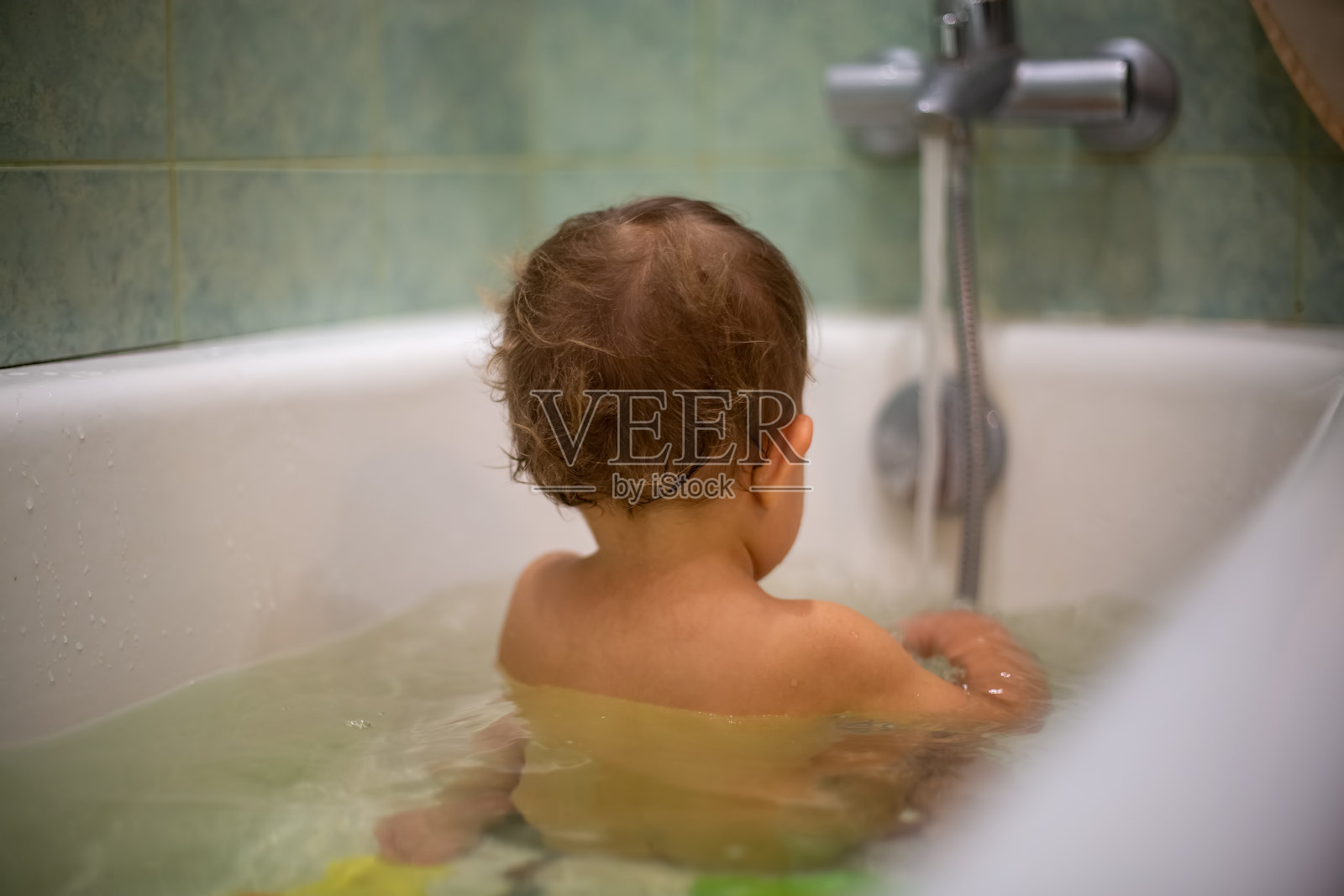 一个可爱的白人婴儿坐在水里洗澡，背对着镜头。特写，软焦点，模糊背景照片摄影图片