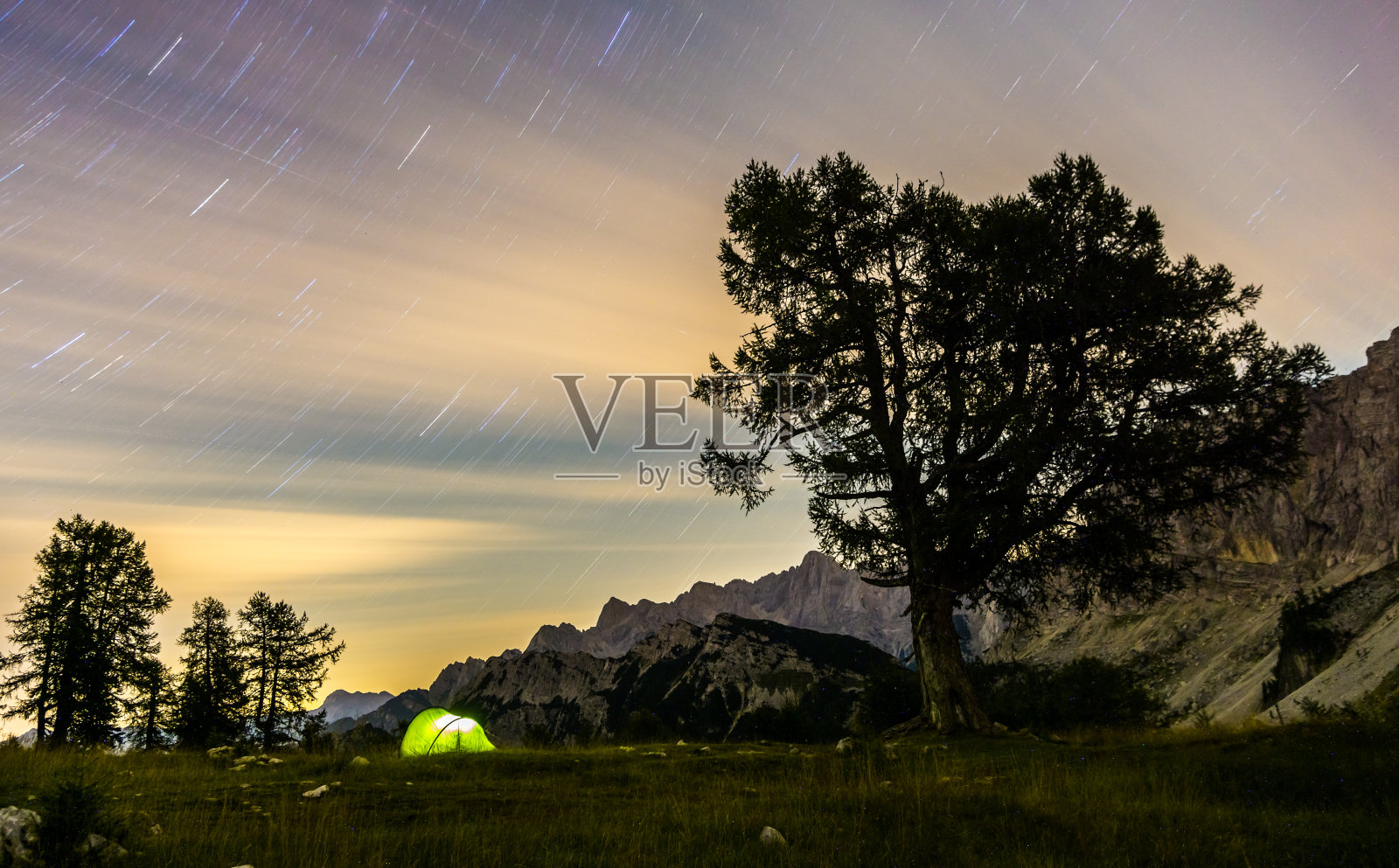 黄昏时分，一个帐篷在星星划过的夜空下闪闪发光。朱利安阿尔卑斯山，特里格拉夫国家公园，斯洛文尼亚，斯雷姆山。照片摄影图片