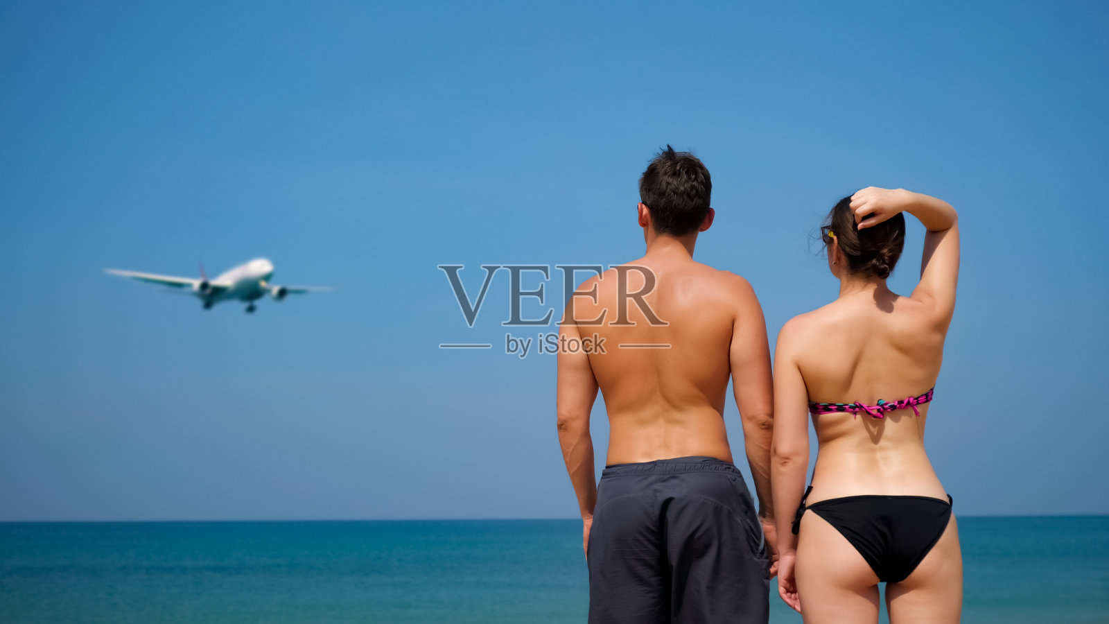 男人和女人站在海边，看着正在接近的飞机照片摄影图片