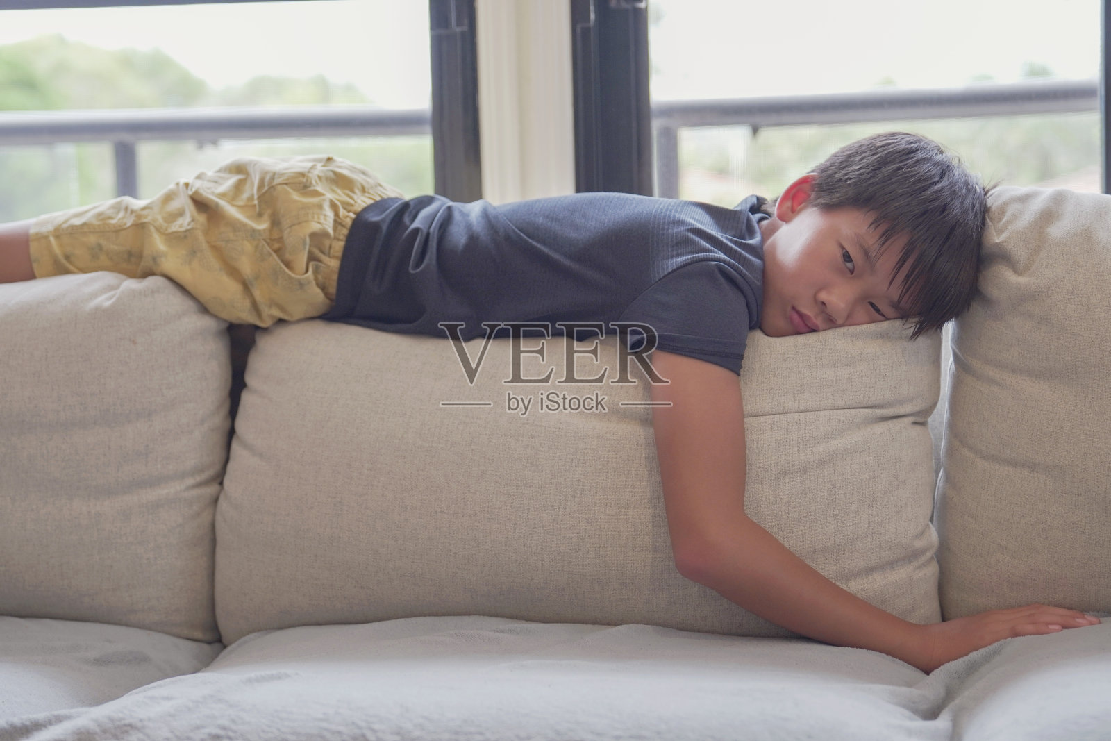 混血亚洲少年躺在家里的沙发上感到无聊，社交距离，隔离，隔离概念，自闭症意识，心理健康照片摄影图片