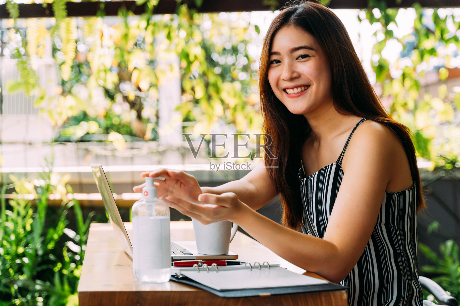 年轻的20多岁的亚洲美丽的女人与迷人的微笑使用洗手液洗手。在咖啡馆外使用电脑、笔记本电脑和手机。-冠状病毒预防概念照片摄影图片