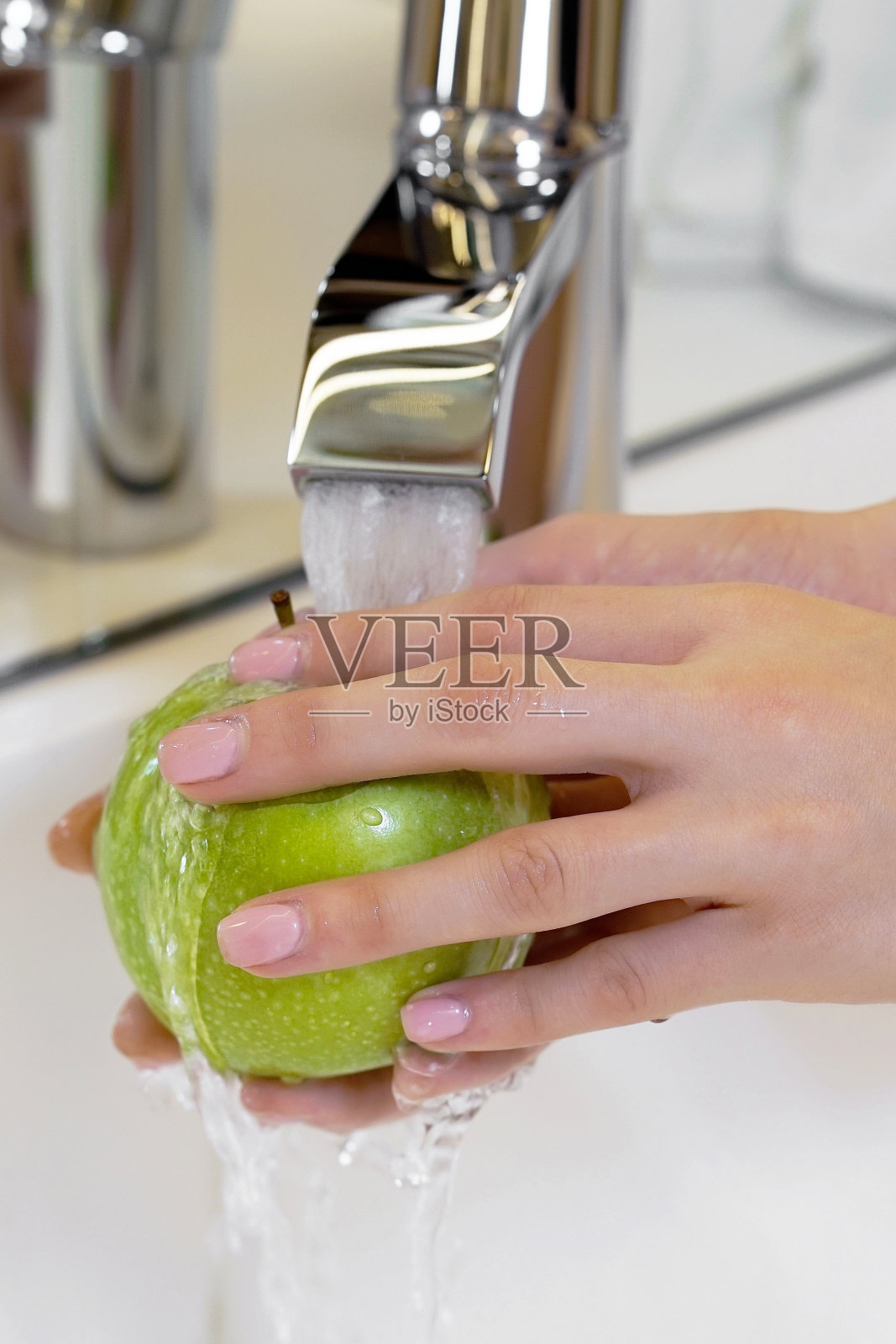 女孩在水龙头下洗青苹果。一位妇女用水龙头里流出的水冲洗着一串青苹果。照片摄影图片
