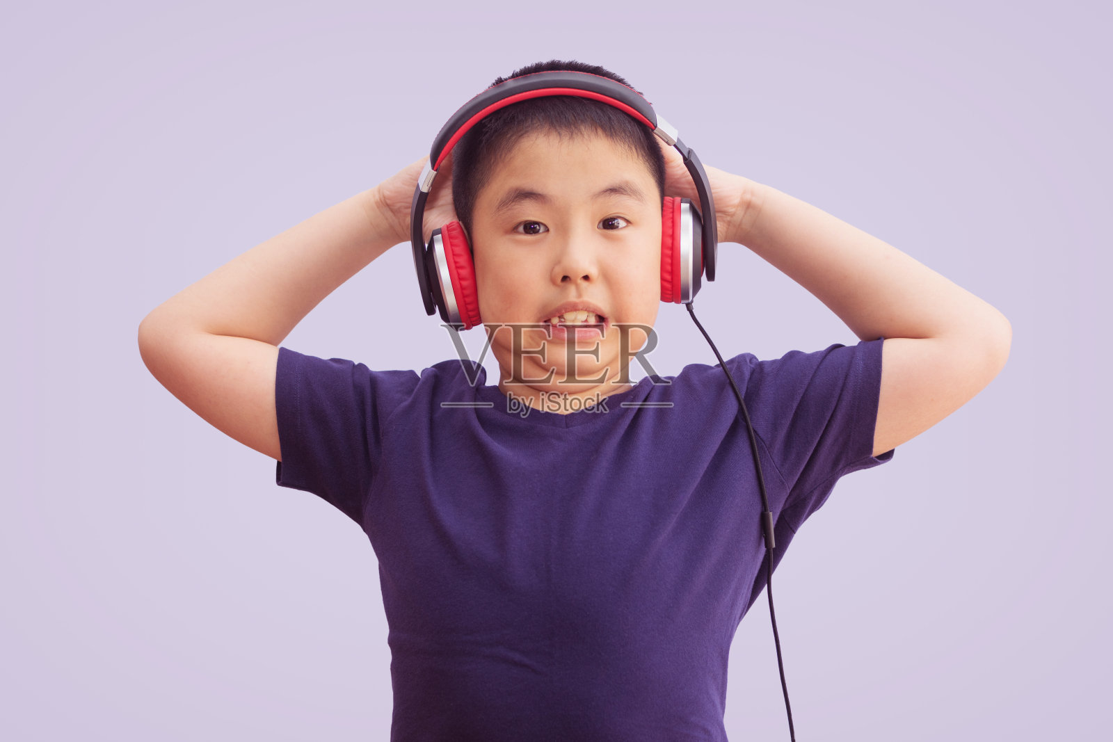 亚洲男孩戴着耳机听着音乐，疯狂而激动地尖叫着，孤立在灰色的背景下照片摄影图片