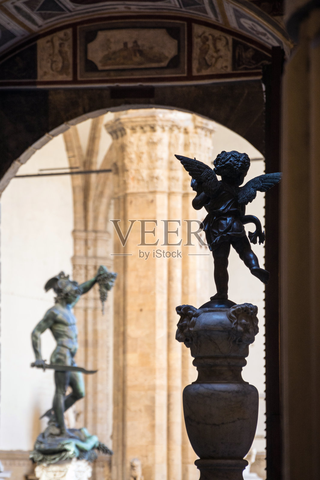 小天使的青铜雕像，背景是珀尔修斯和美杜莎的头，在朗齐走廊，从佛罗伦萨韦基奥宫看到的della Signoria广场。意大利照片摄影图片