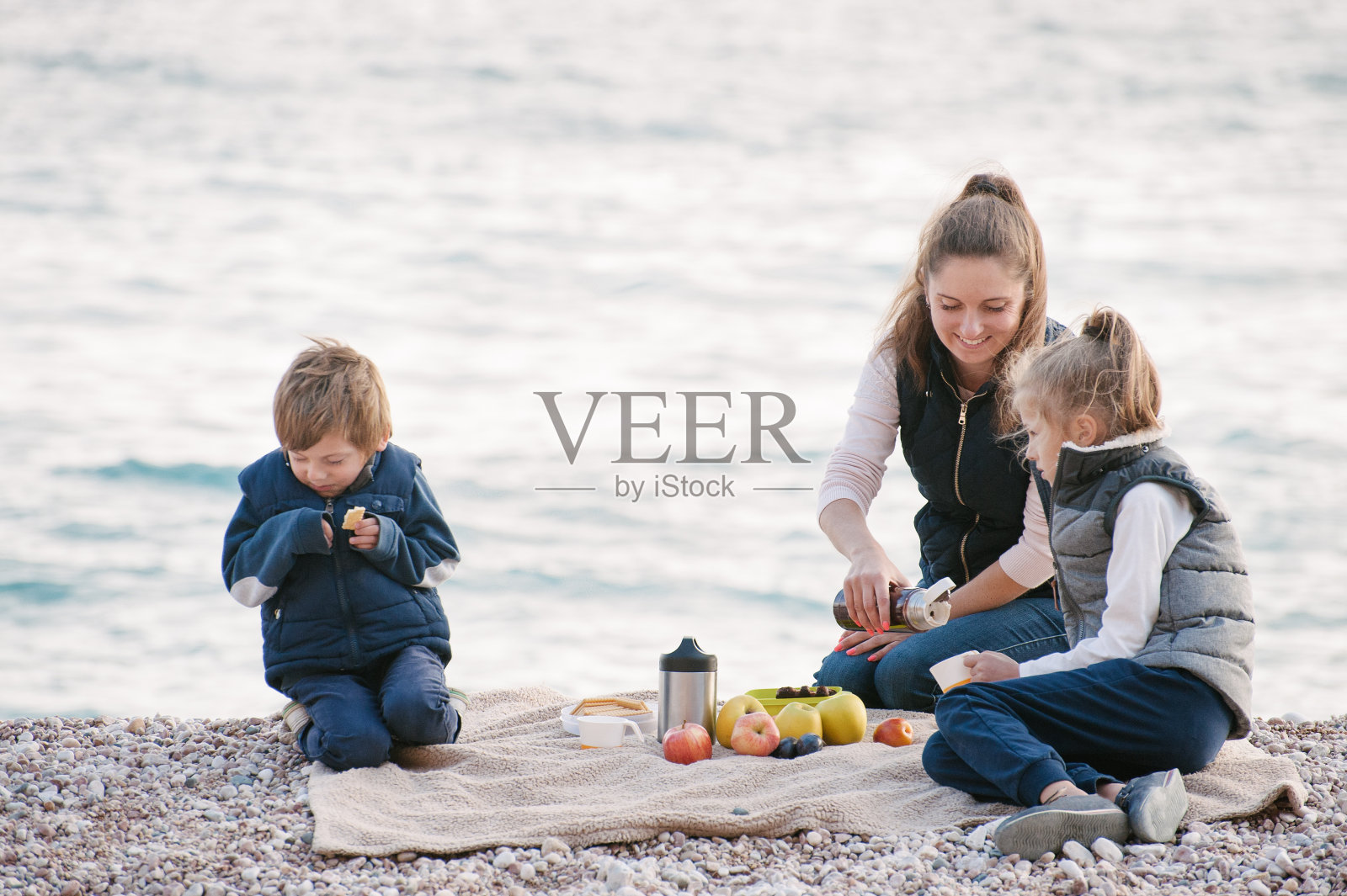 快乐的母亲和两个孩子在海边野餐的秋天照片摄影图片