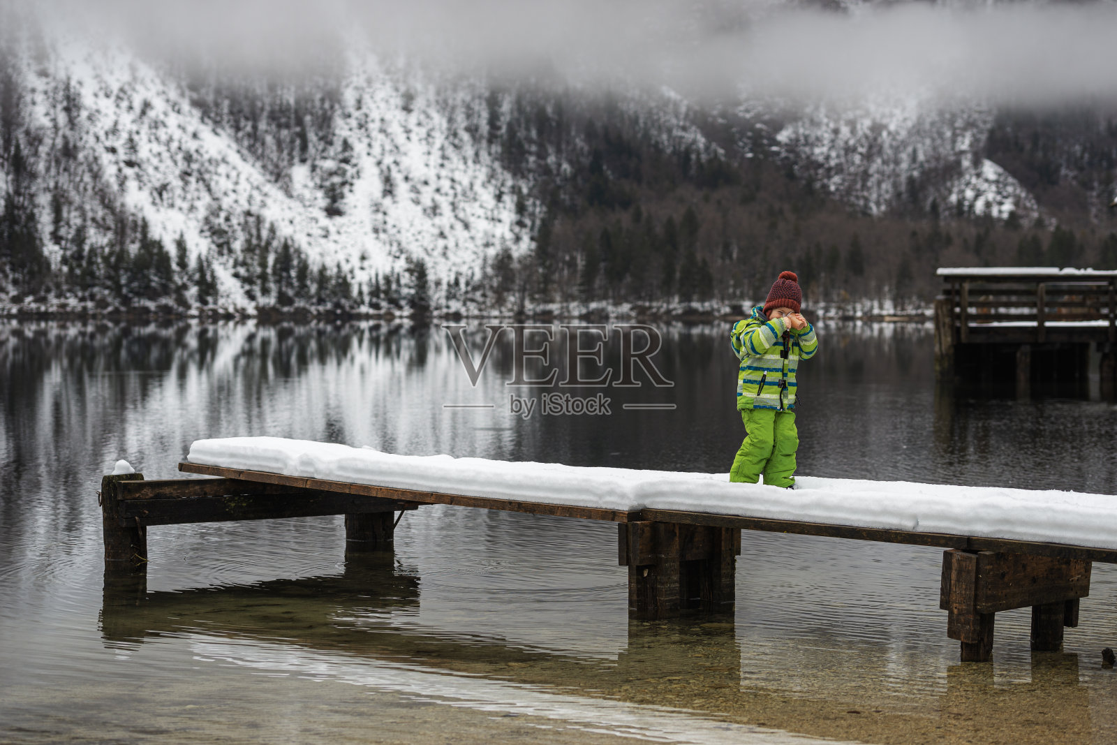 蹒跚学步的男孩站在白雪覆盖的码头上照片摄影图片