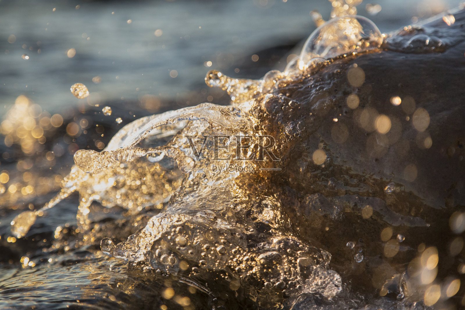 近景照片的海浪刹车在潮湿的海滨石头夏季日落，水溅，阳光，反射在水滴。照片摄影图片