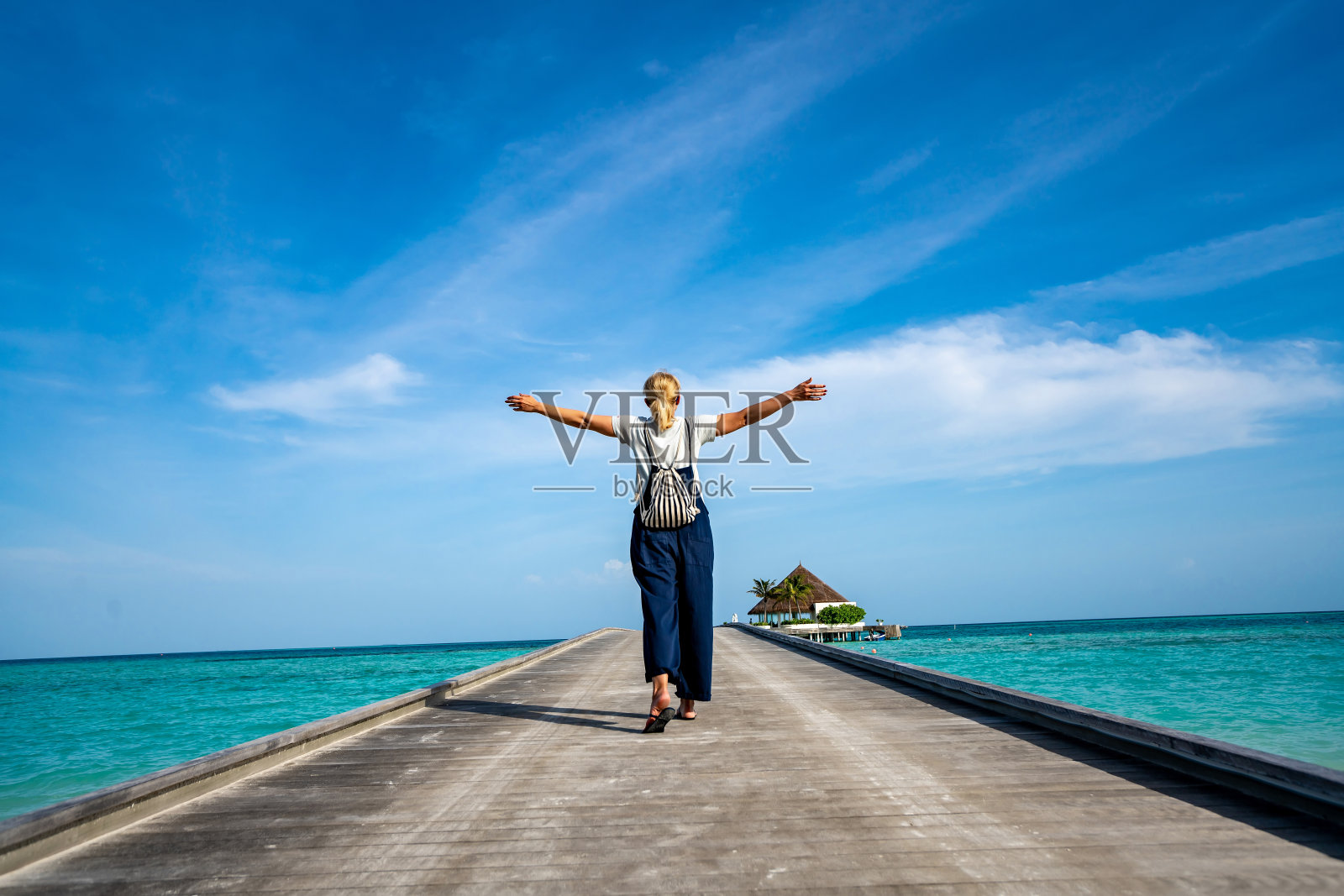 快乐的女人走在以碧海蓝天为背景的木栈桥上。照片摄影图片