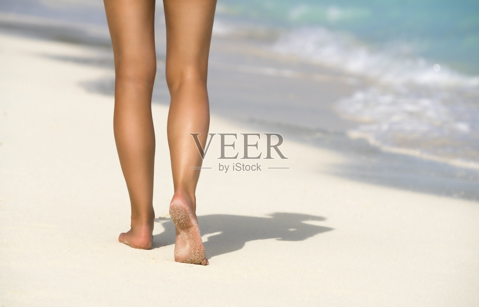在热带海滩上的蓝色海水中的女性脚的特写。假期假期。照片摄影图片
