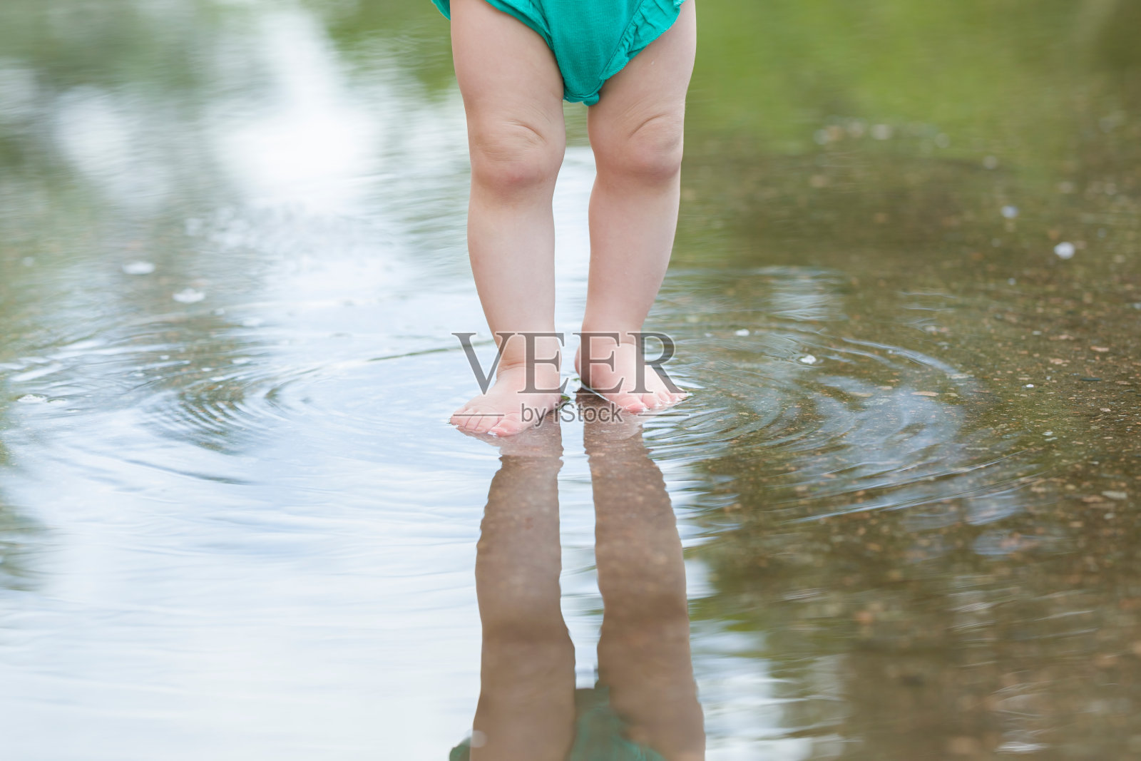 温暖的雨后，婴儿的腿站在浅水坑里。前视图。光脚的特写镜头。照片摄影图片