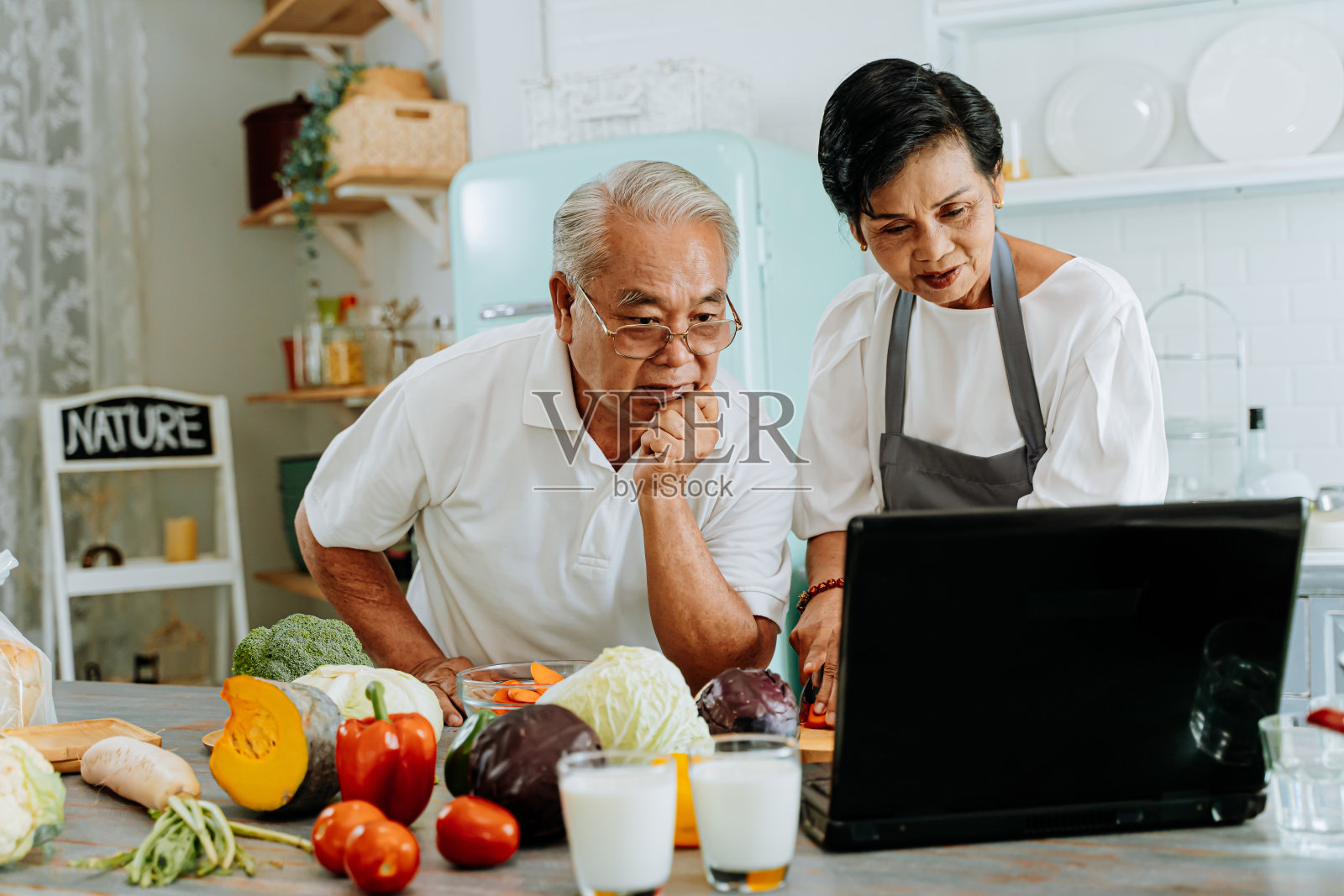 一对亚洲老年夫妇在家做饭时使用笔记本电脑。70年代老年男女关系退休生活方式概念照片摄影图片