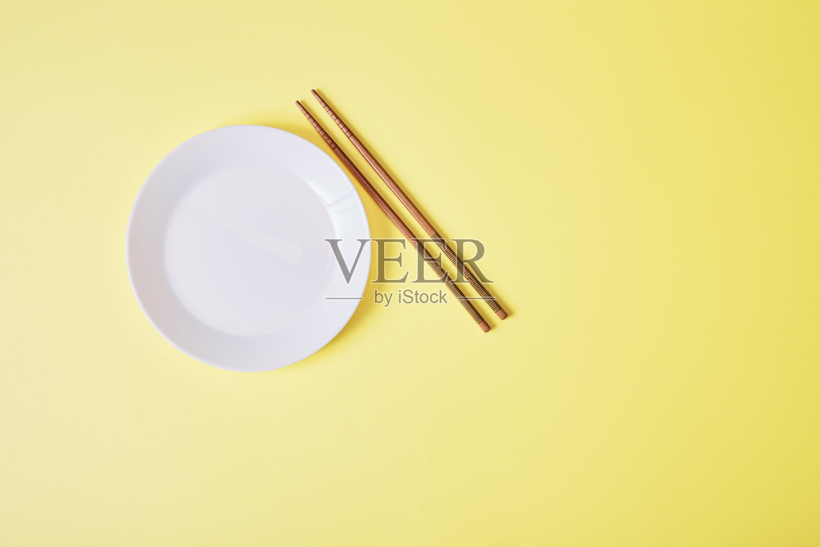 黄色背景上用木筷子夹空白色盘子照片摄影图片