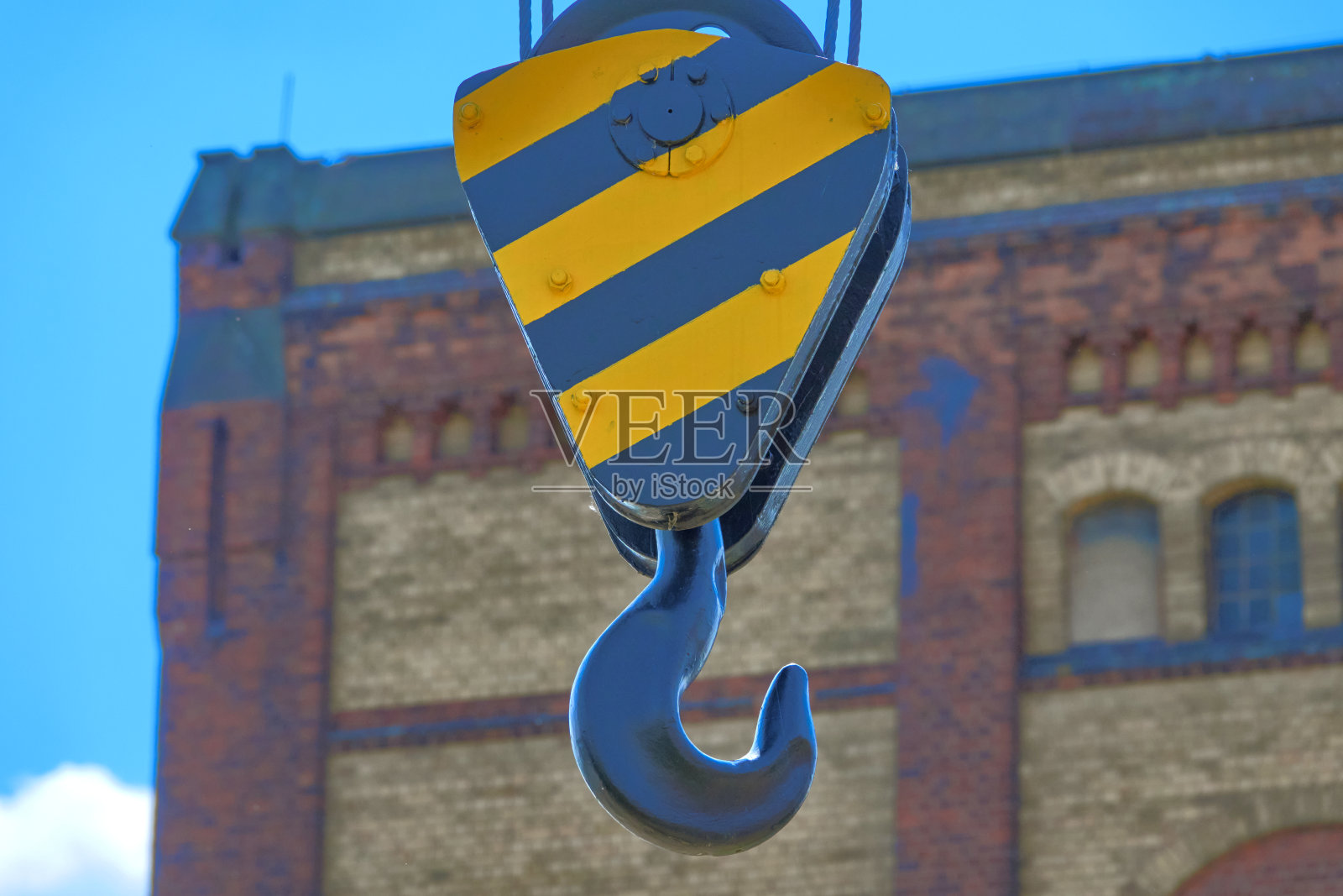 一个黑色和黄色的重型铁钩固定在一个故意模糊的工业建筑立面前照片摄影图片