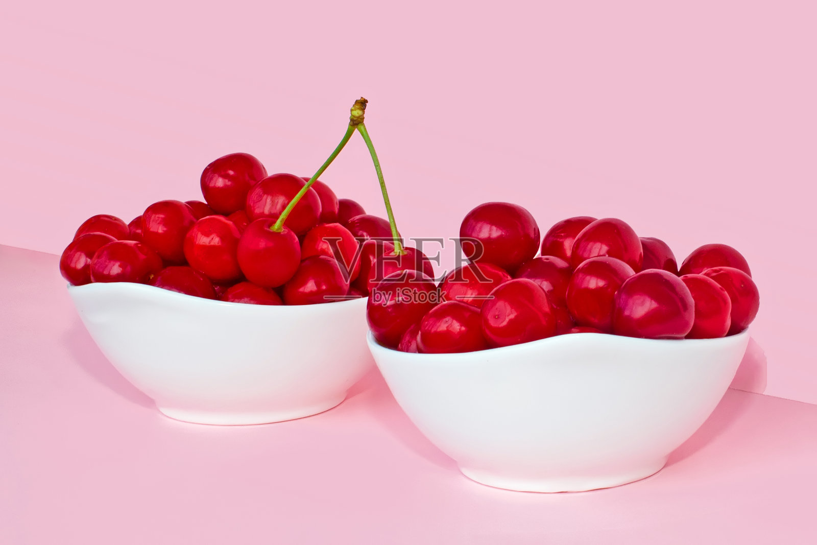 两碗樱桃浆果，粉色背景。夏天的概念。照片摄影图片