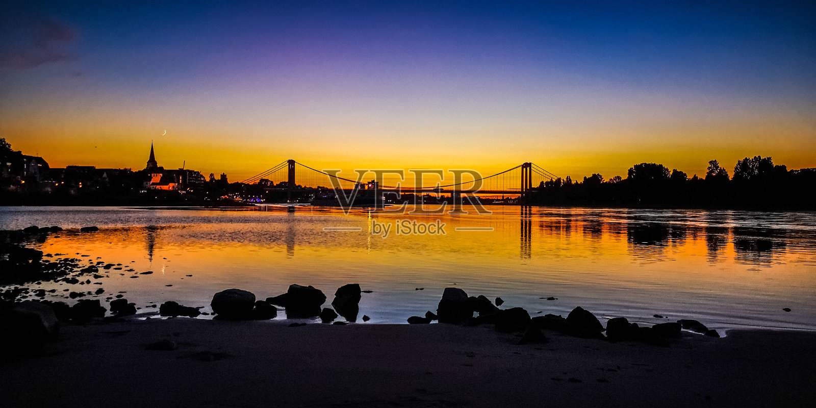 日落在科隆莱茵河河畔的沙滩上，天空和阳光反射和桥照片摄影图片