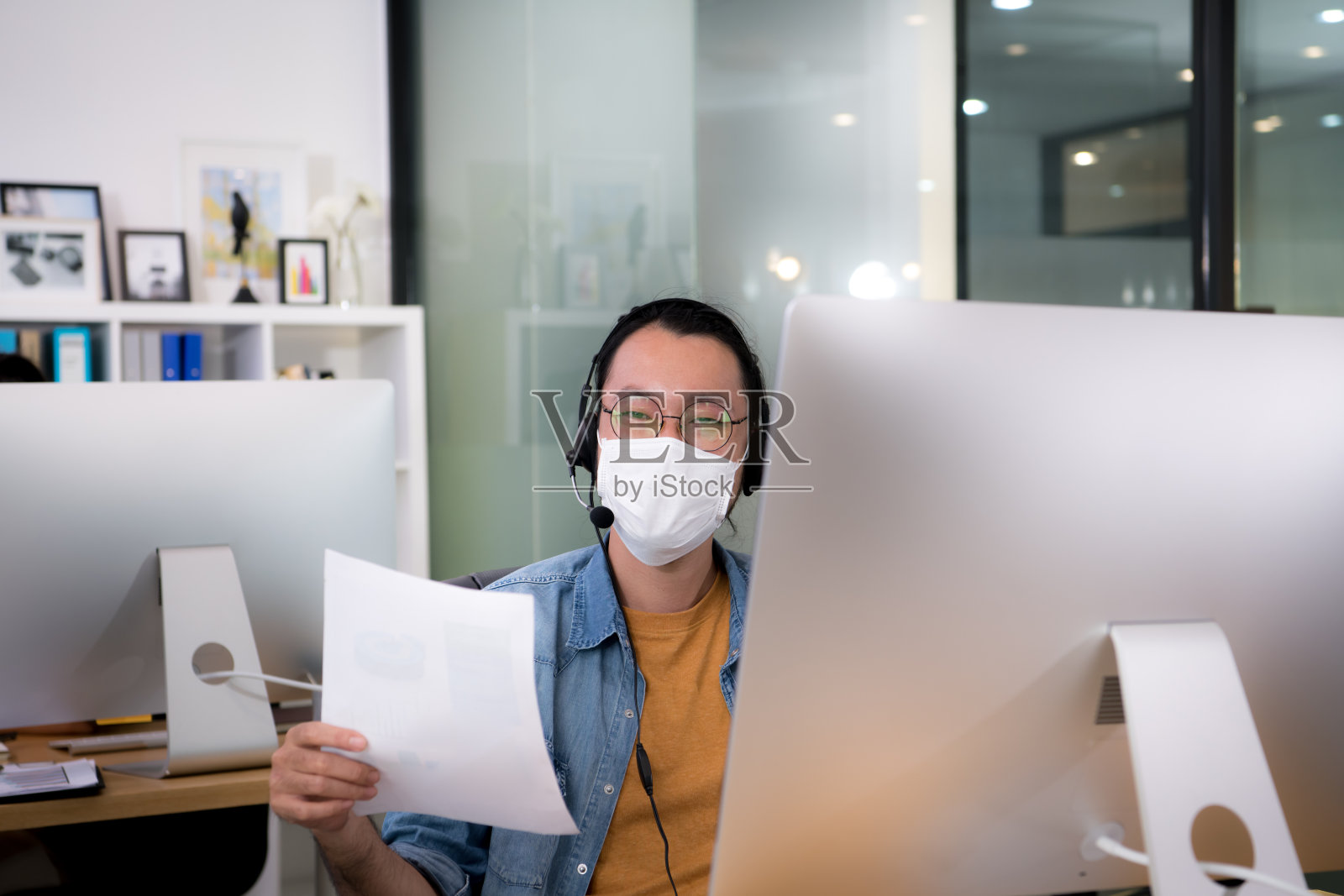 在新冠肺炎大流行期间，亚洲白领戴着口罩在新常态的办公室工作，并保持社交距离照片摄影图片