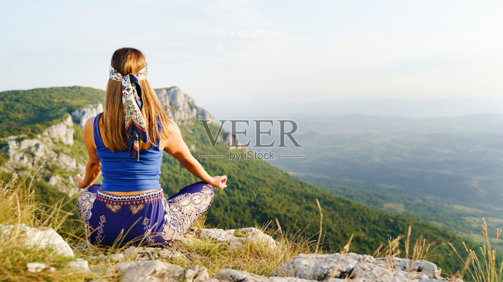 在夏秋之日，白种女子以莲花瑜伽姿势坐在山顶悬崖上的背影——冥想和放松灵性概念的复制空间照片摄影图片