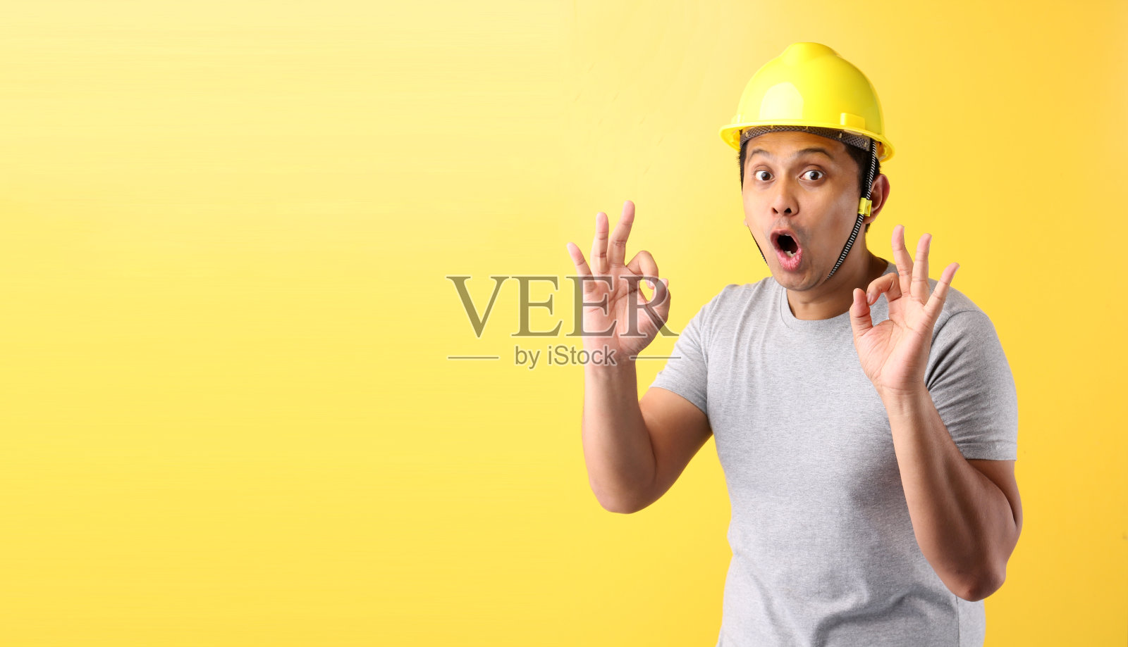 亚洲人工业工人或工程师，在建筑建造商工作，在工作室的黄色背景上显示ok手势与复制空间，概念国际劳动节。照片摄影图片