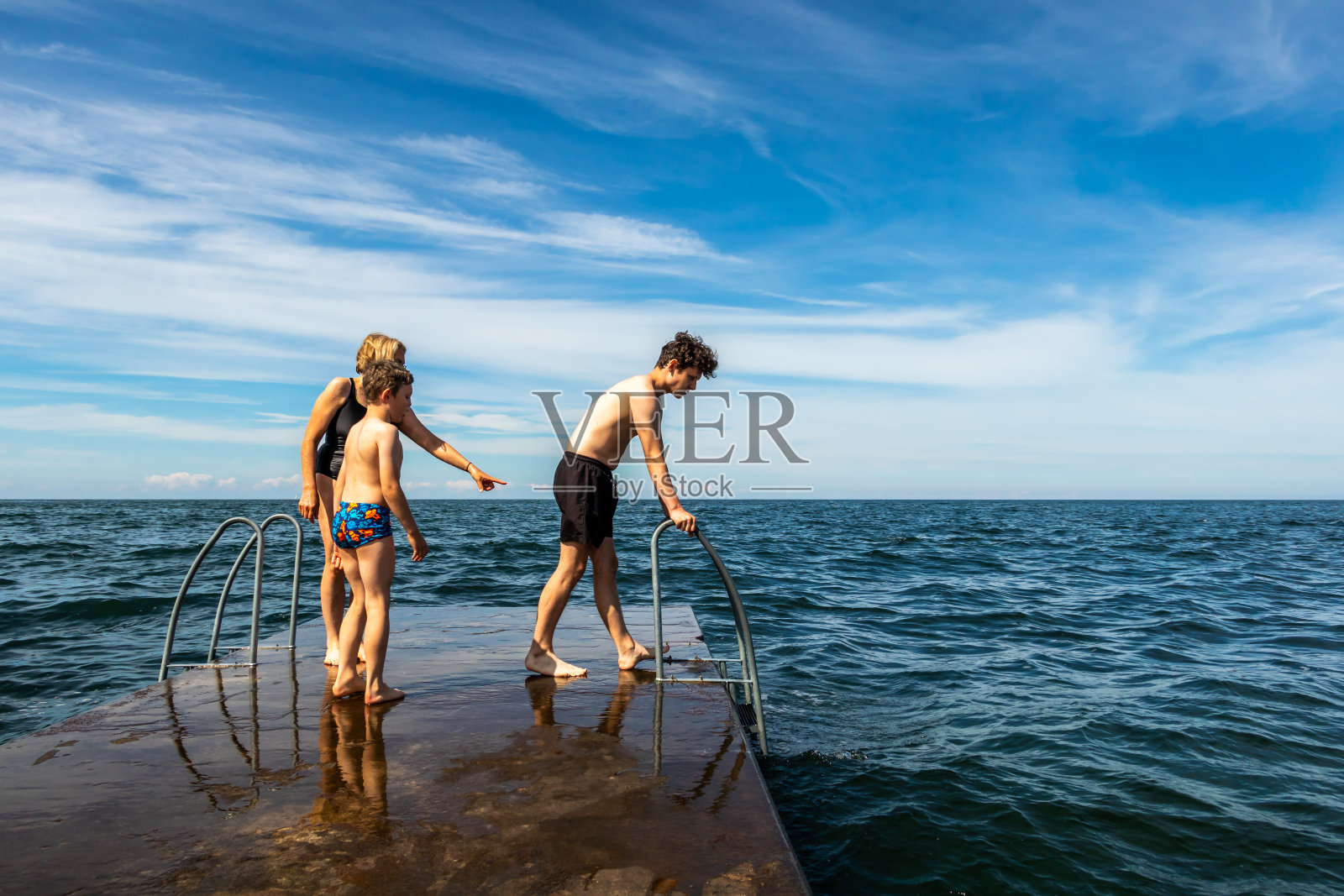 夏天的观点，一个家庭在一个石头码头上即将游泳在波罗的海的海洋与蓝天和地平线。照片摄影图片