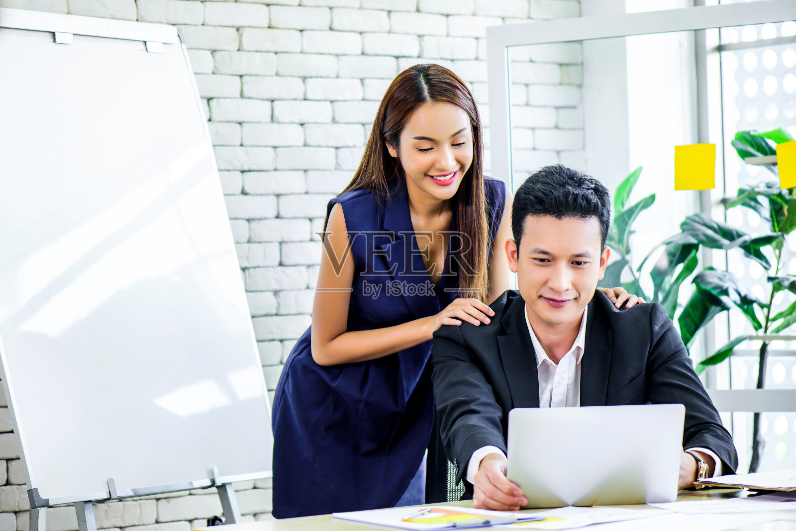 年轻的亚洲夫妇一起工作使用笔记本电脑在现代办公室与复印空间。中小企业企业家，商业伙伴，爱情关系，或自由职业者的概念照片摄影图片