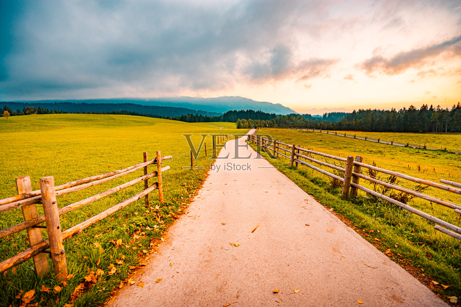 德国巴伐利亚乡村的一条乡村公路。绿色草地和路径在前景与戏剧性的日落天空和云彩在背景照片摄影图片