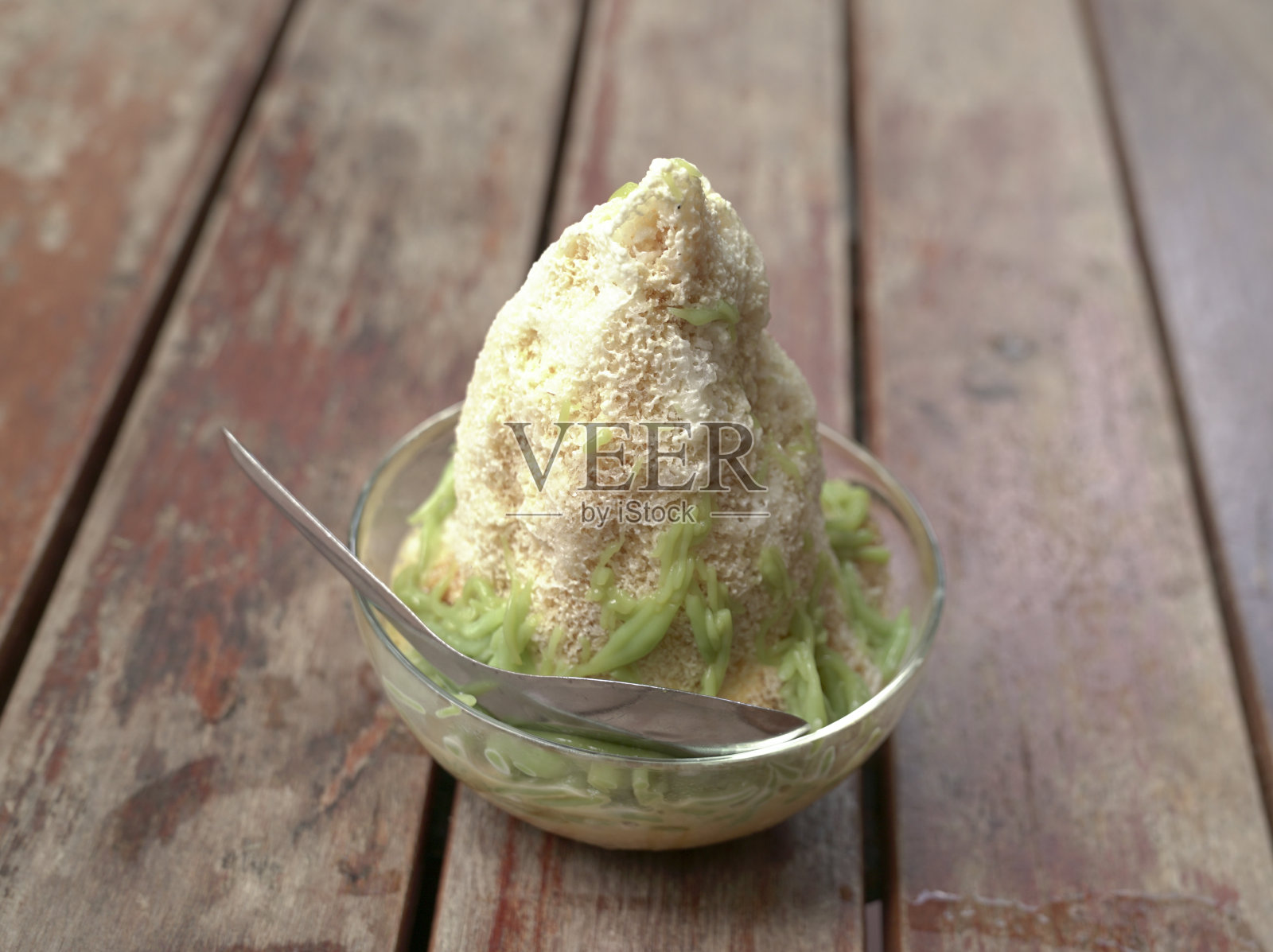 Cendol，甜刨冰和绿色米粉果冻放在一个碗里，放在一张木桌上照片摄影图片
